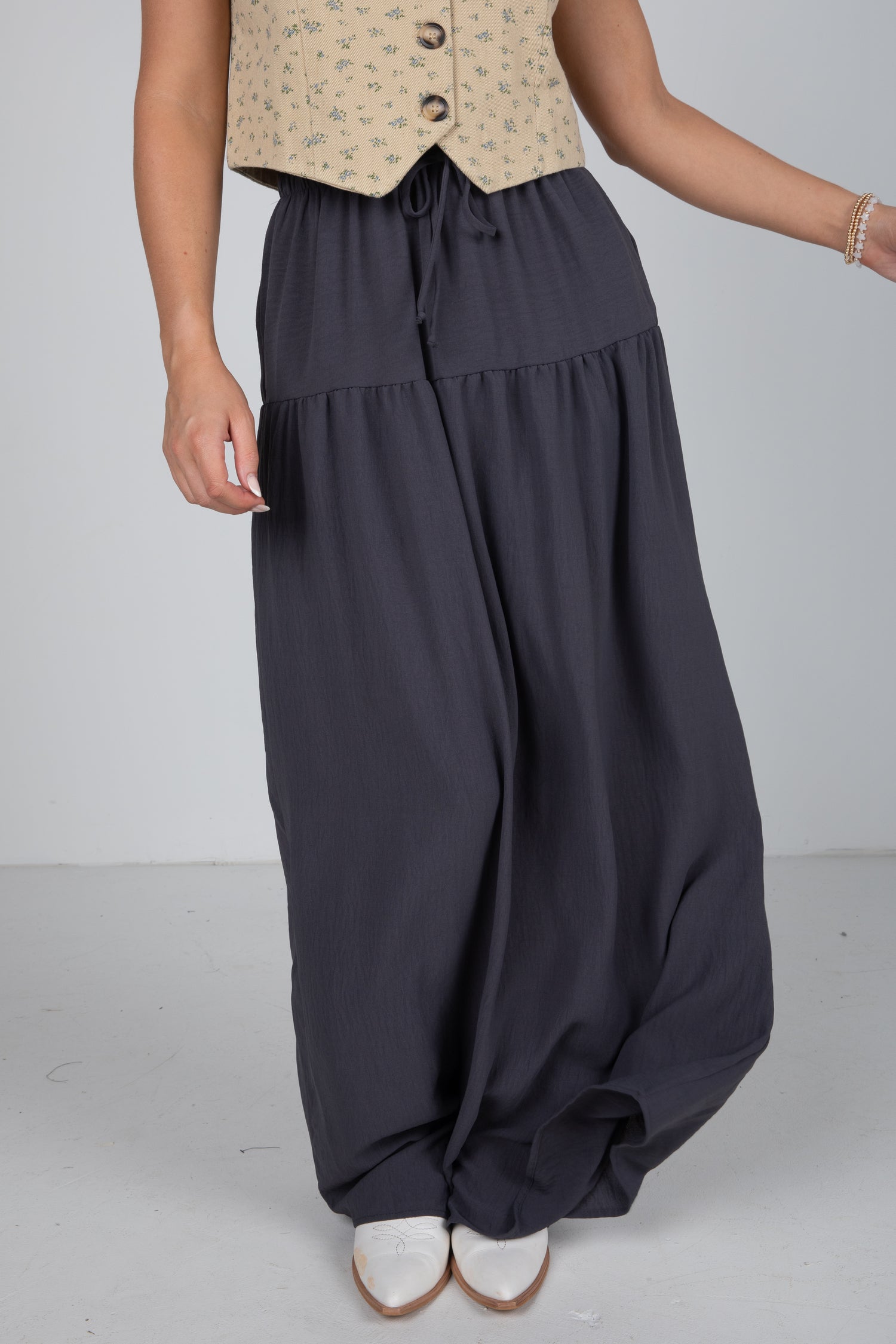 Person wearing dark gray wide-leg pants with a beige top on a plain background