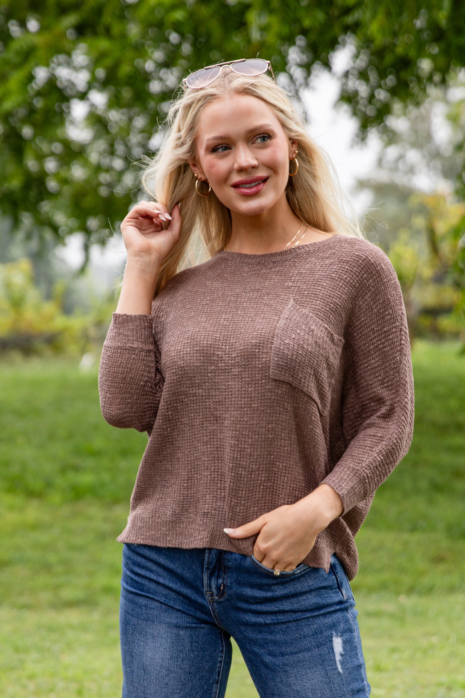 Woman wearing a brown sweater and blue jeans outdoors