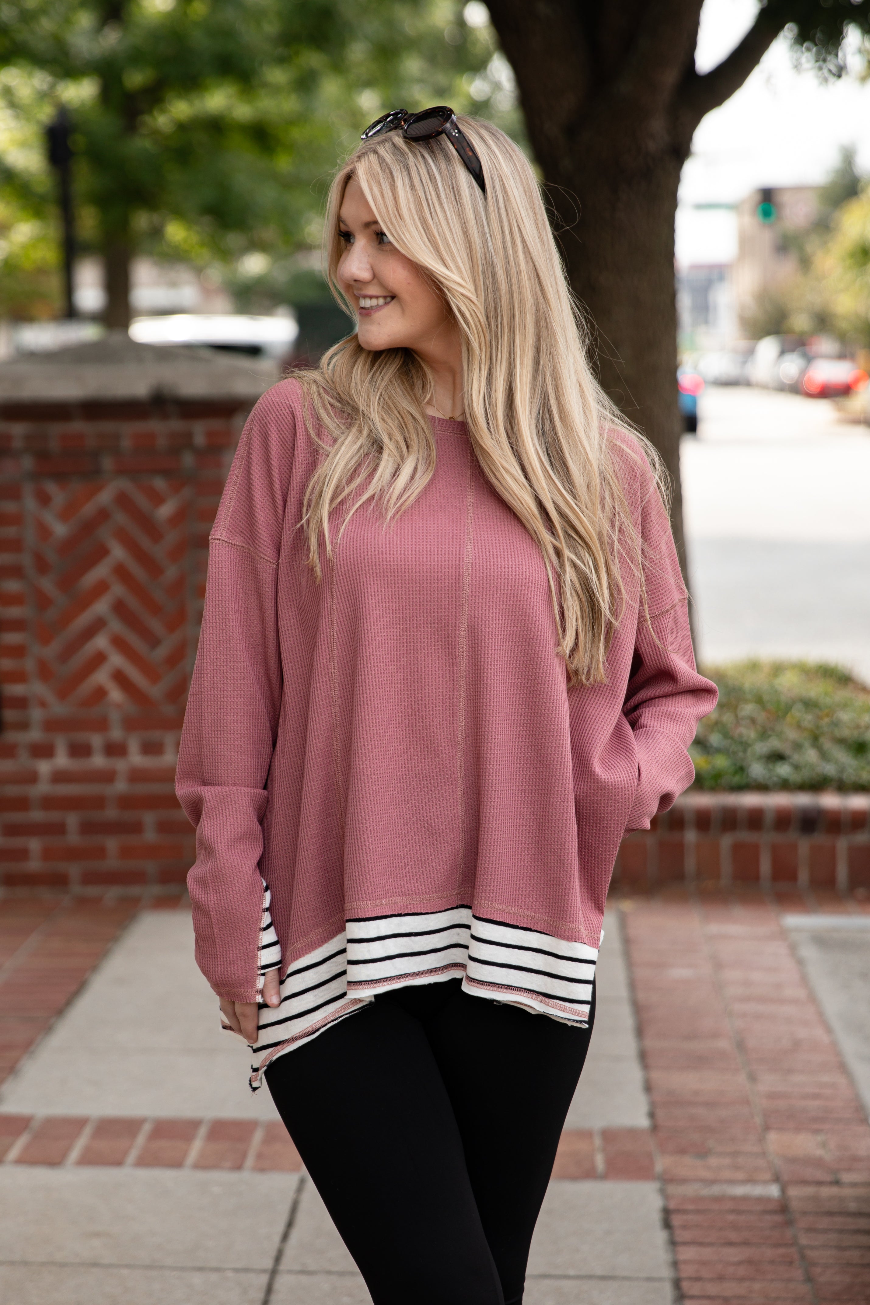 Woman wearing a pink sweater with a striped hem on a city street.