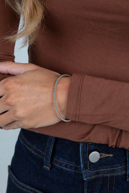 Close-up of a person wearing a brown jacket and blue jeans with a bracelet on a light gray background