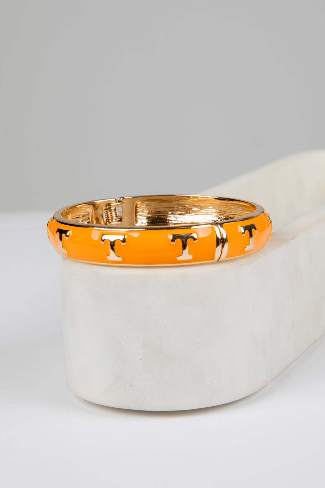Gold and orange bracelet with horse design on a white surface