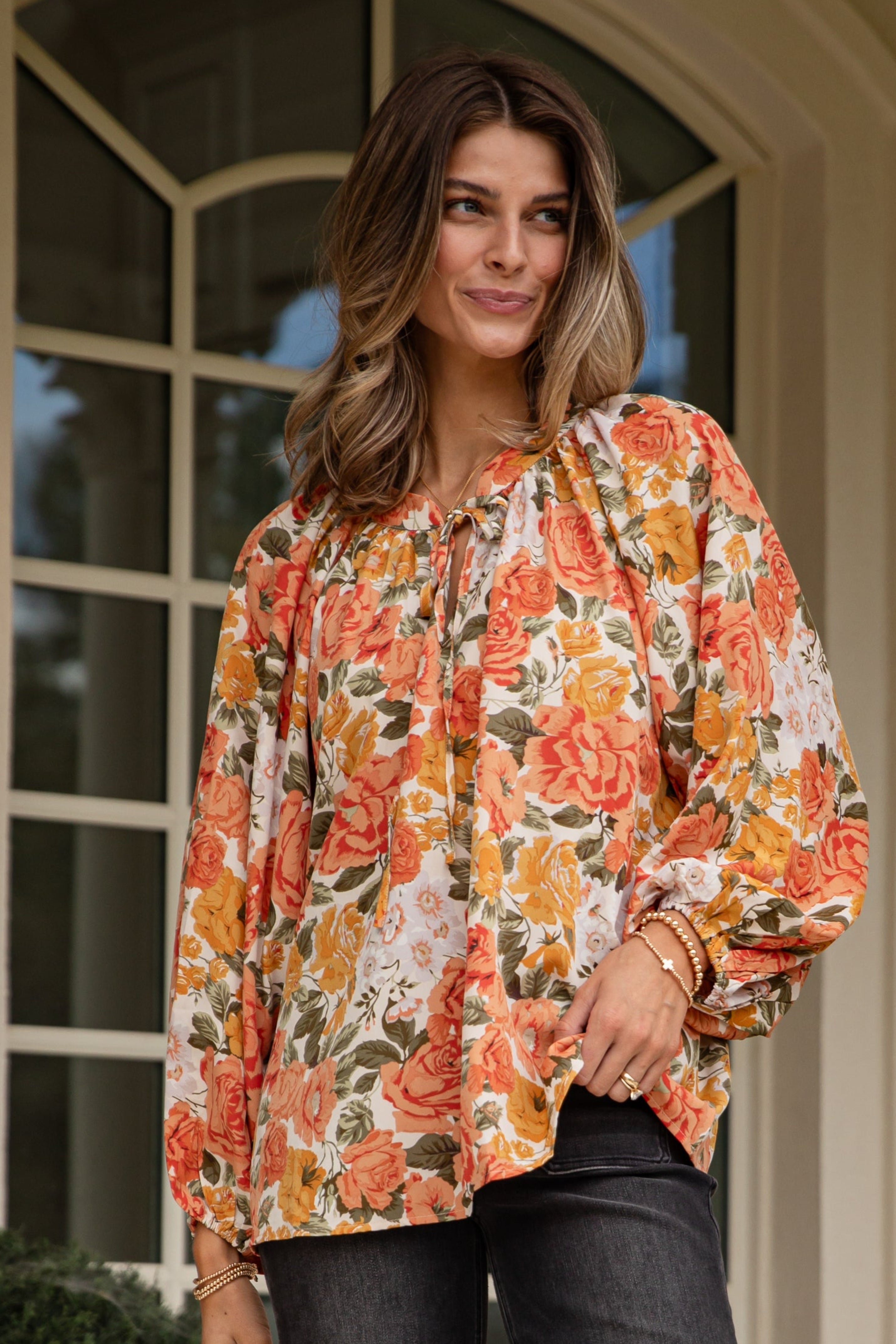 Woman wearing a floral blouse and dark jeans standing on a porch.
