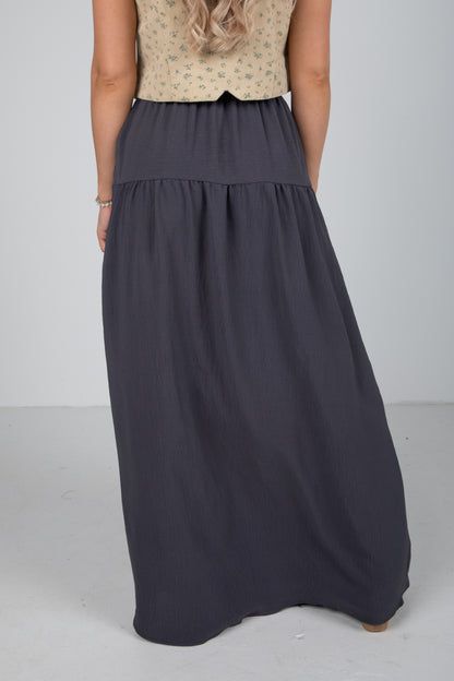 Person wearing a long dark gray skirt on a plain background