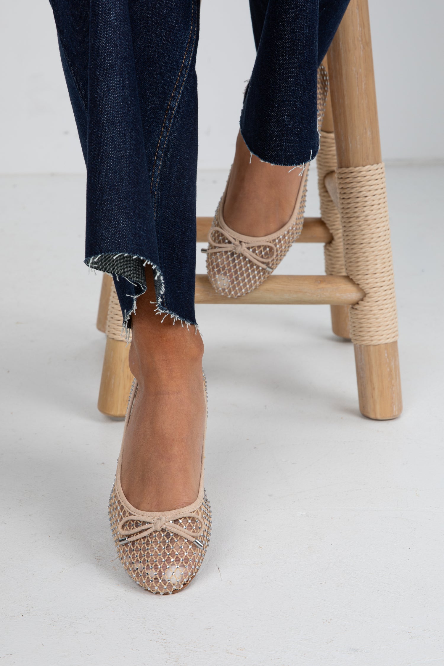 Beige espadrille shoes worn with dark jeans on a light background
