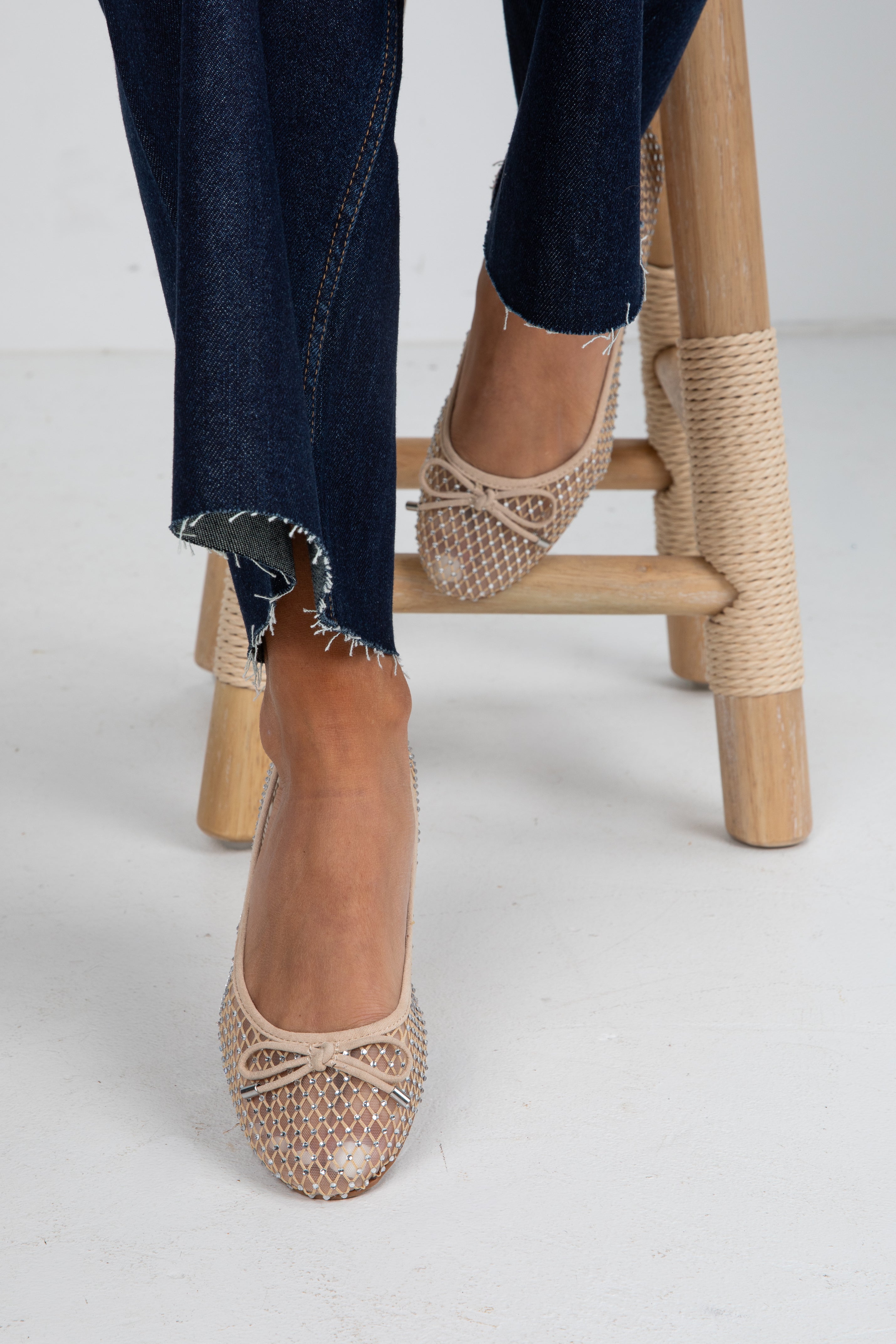 Beige espadrille shoes worn with dark jeans on a light background