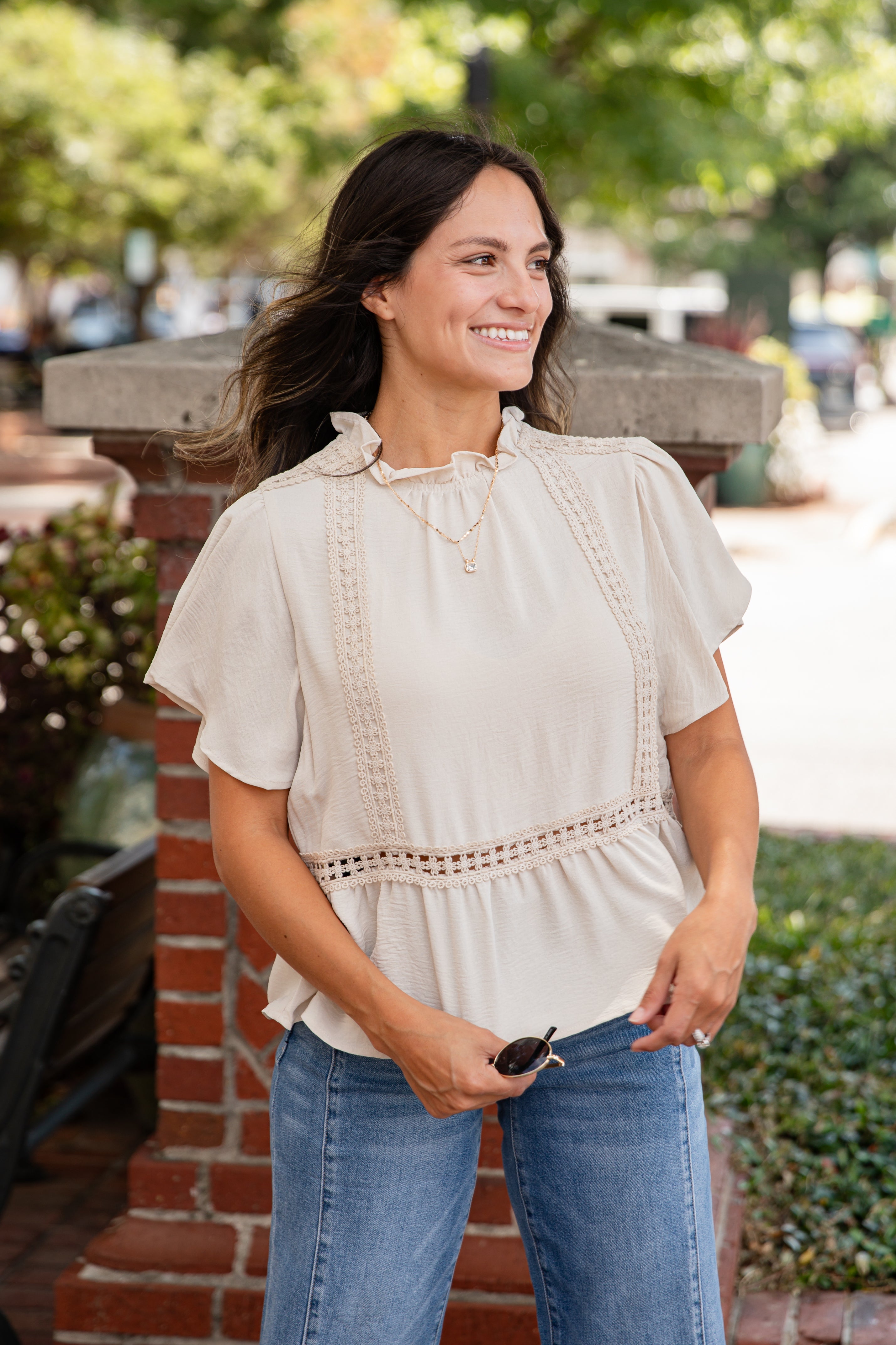 Woman wearing a beige blouse and blue jeans standing outdoors.
