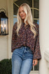Woman standing on a porch wearing a patterned blouse and blue jeans.