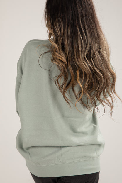 Person wearing a light green hoodie with long wavy hair on a plain background