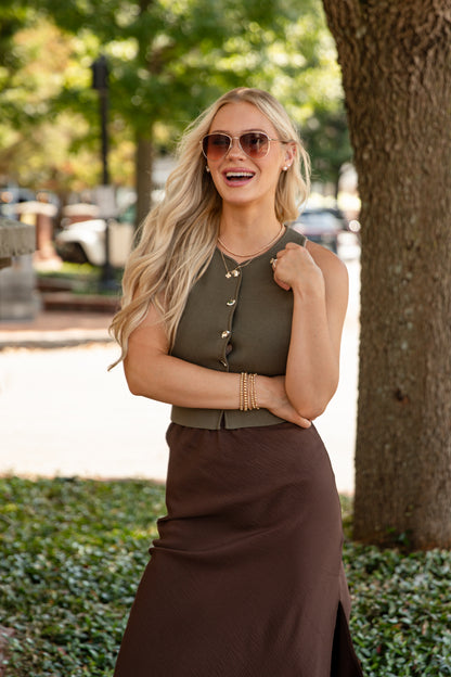 Woman wearing sunglasses and a green top with a brown skirt standing outdoors.
