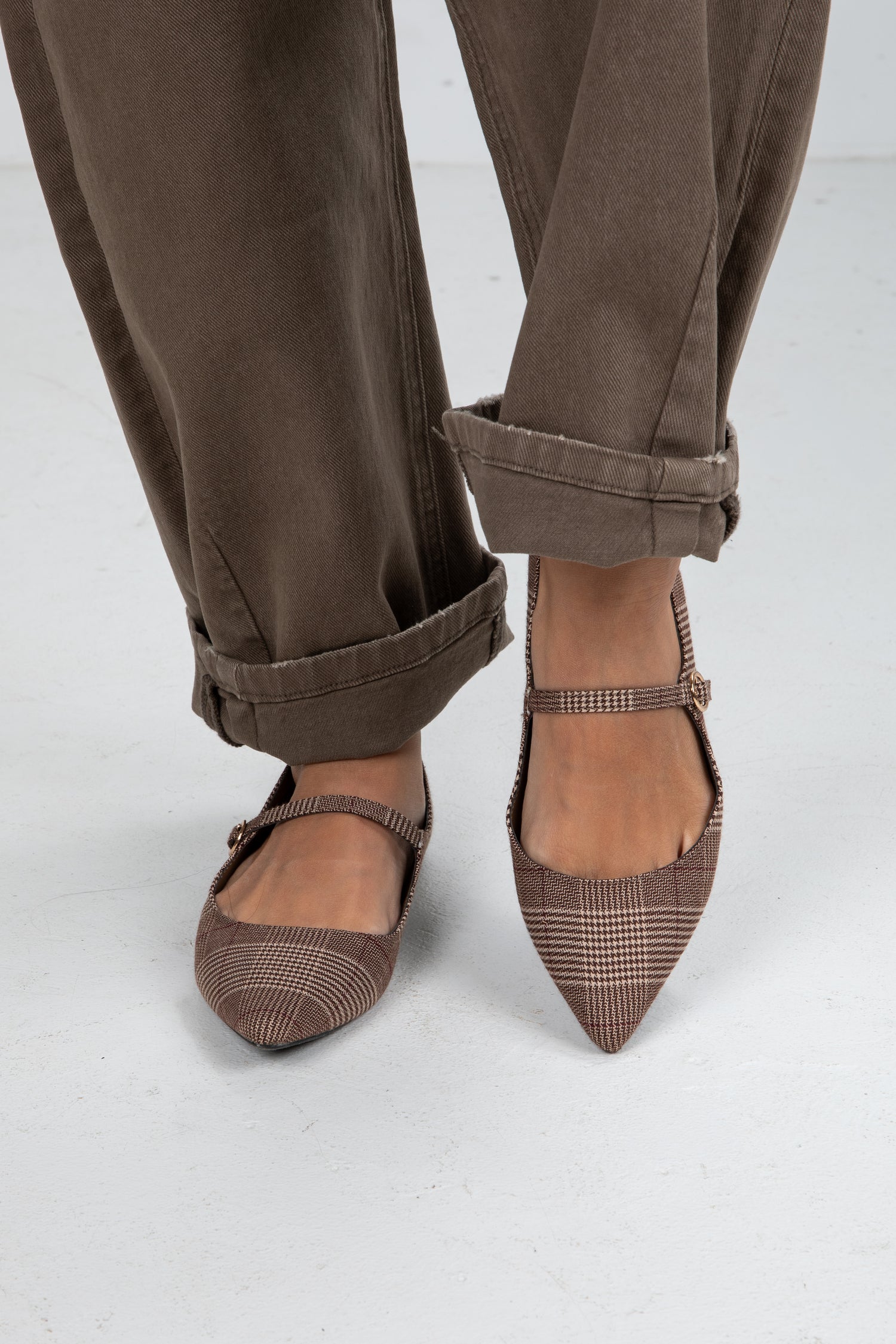 Brown checkered shoes worn with brown pants on a white background