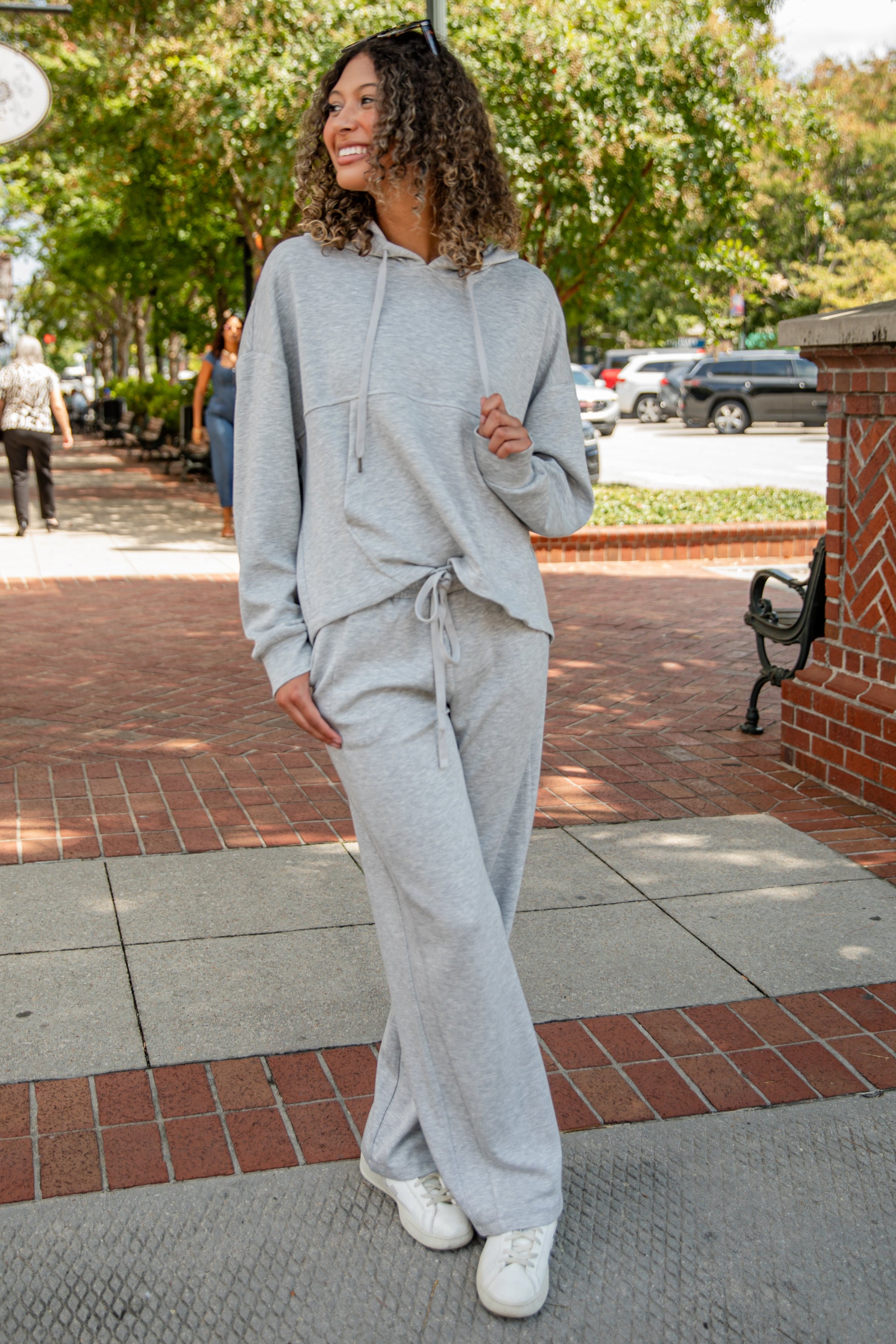 Woman in gray tracksuit walking on a sidewalk with trees and buildings in the background