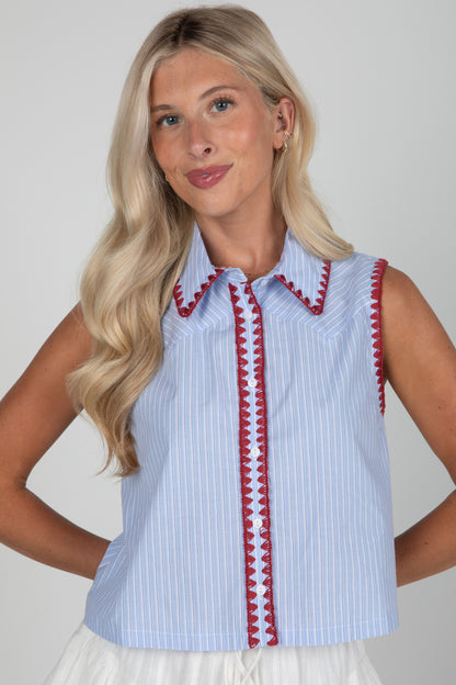 Woman wearing a sleeveless blue and white striped shirt with red trim on a plain background