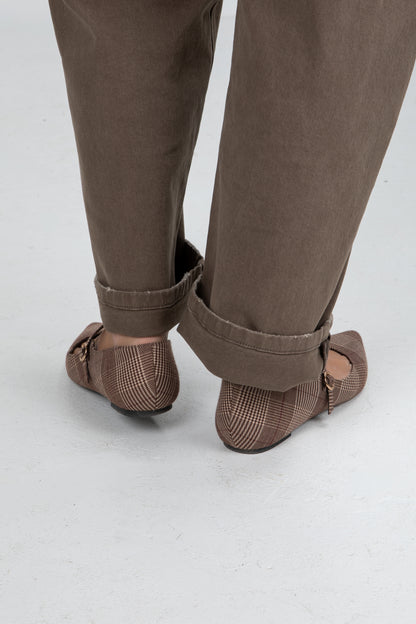 Brown shoes worn with rolled-up brown pants on a white background
