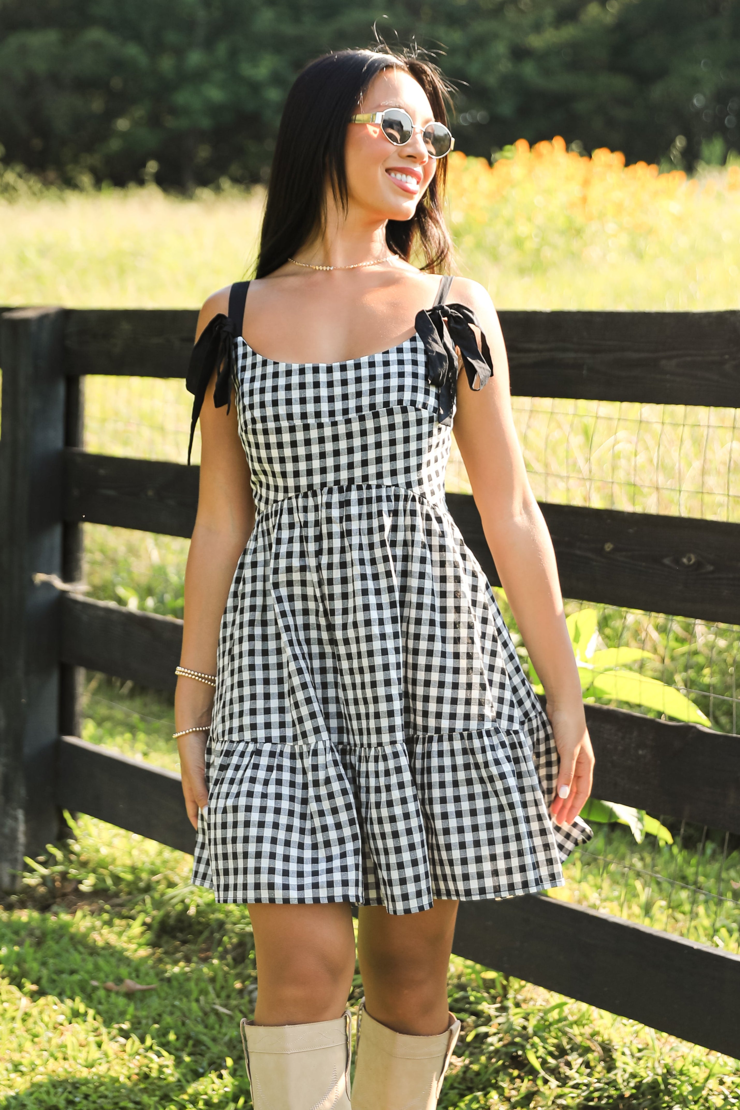 Woman in a checkered dress standing in a field with a wooden fence.