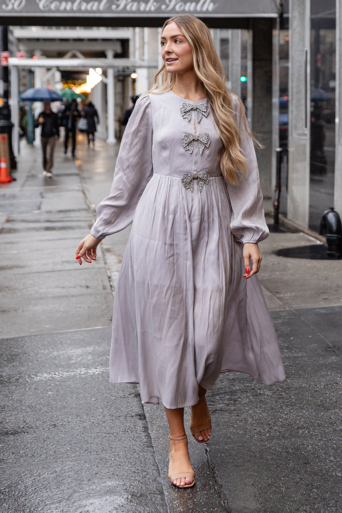 Woman in a light gray dress walking on a city street with &