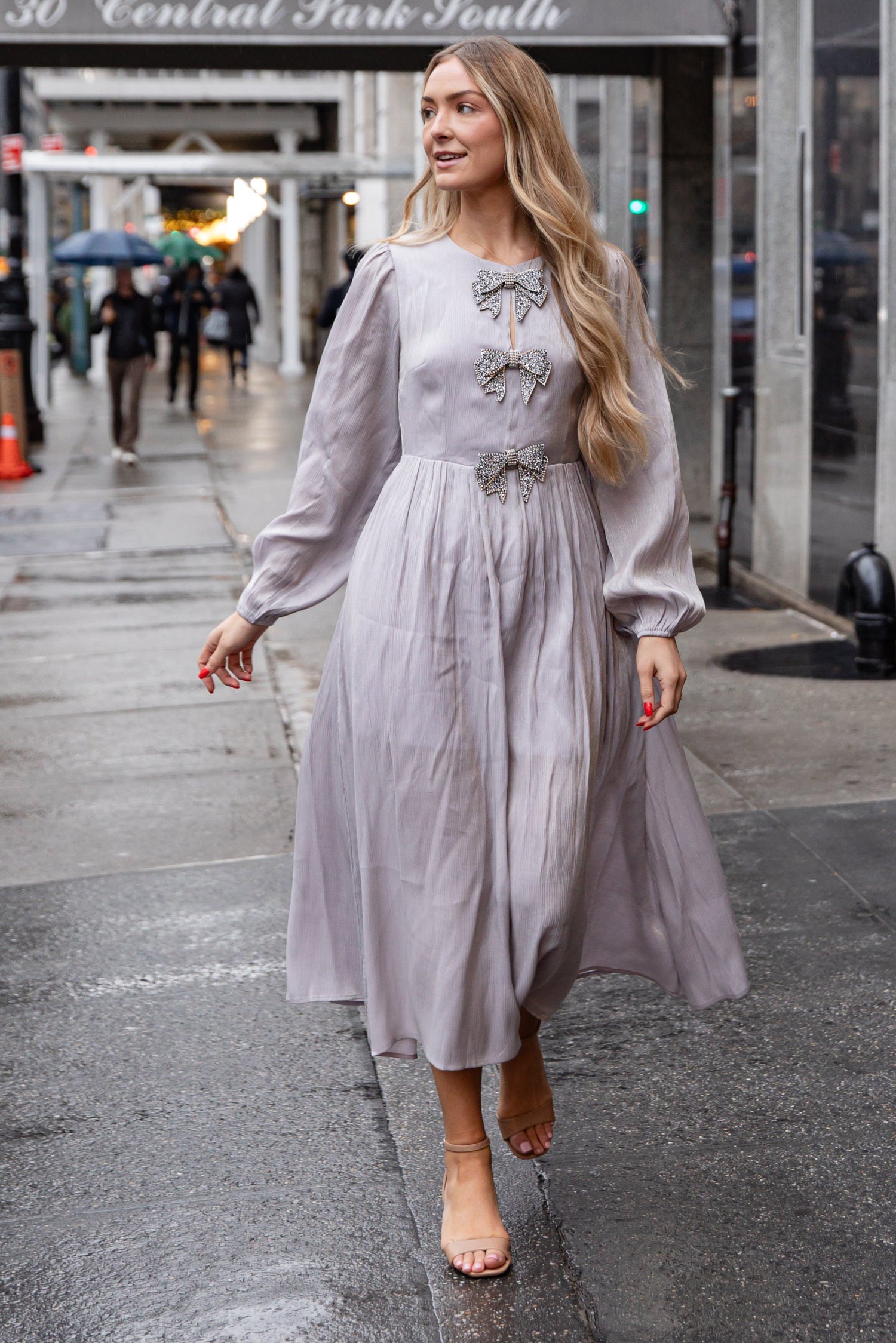 Woman in a light gray dress walking on a city street with &