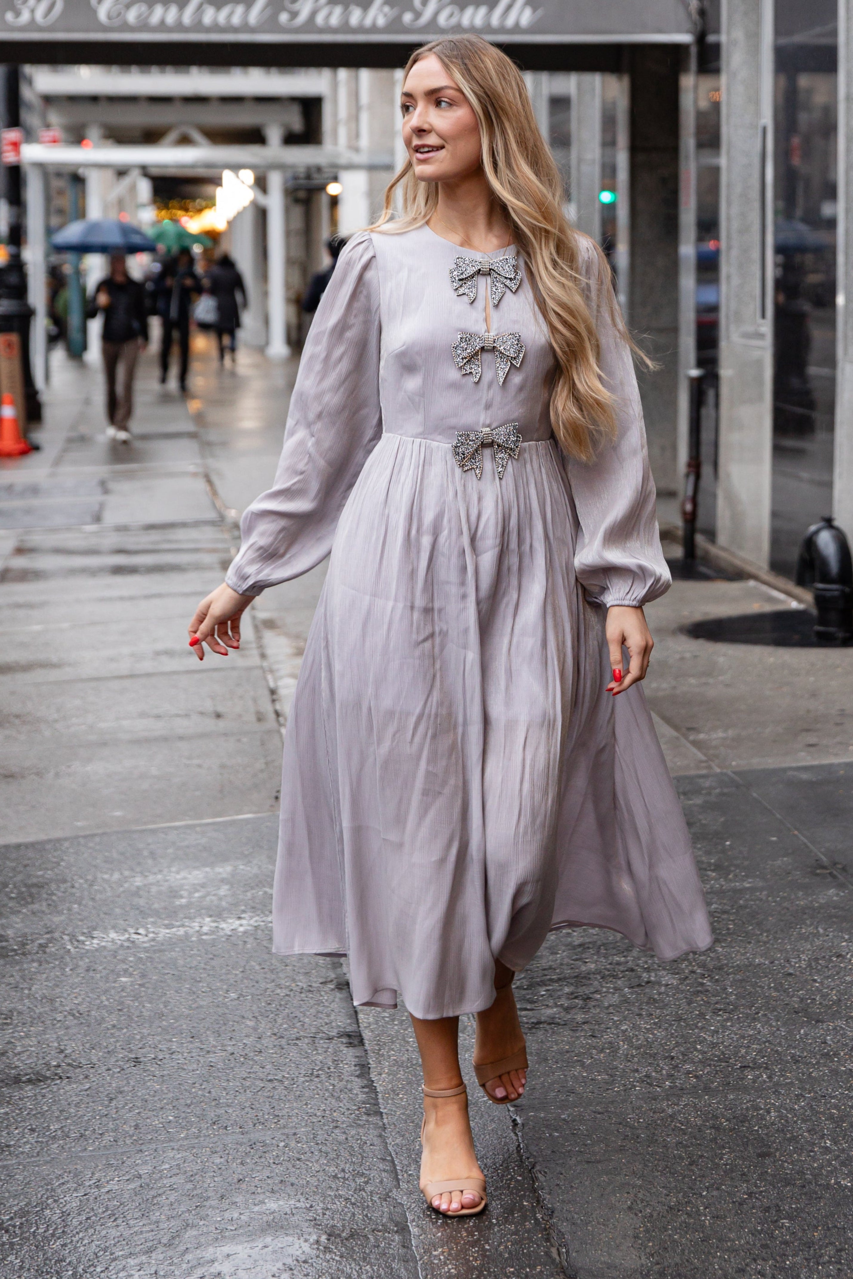 Woman in a light gray dress walking on a city street with &