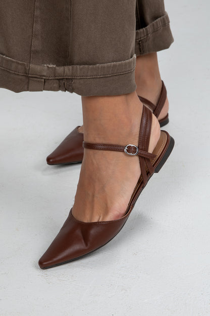Brown pointed-toe shoes with thin straps worn by a person on a light gray background