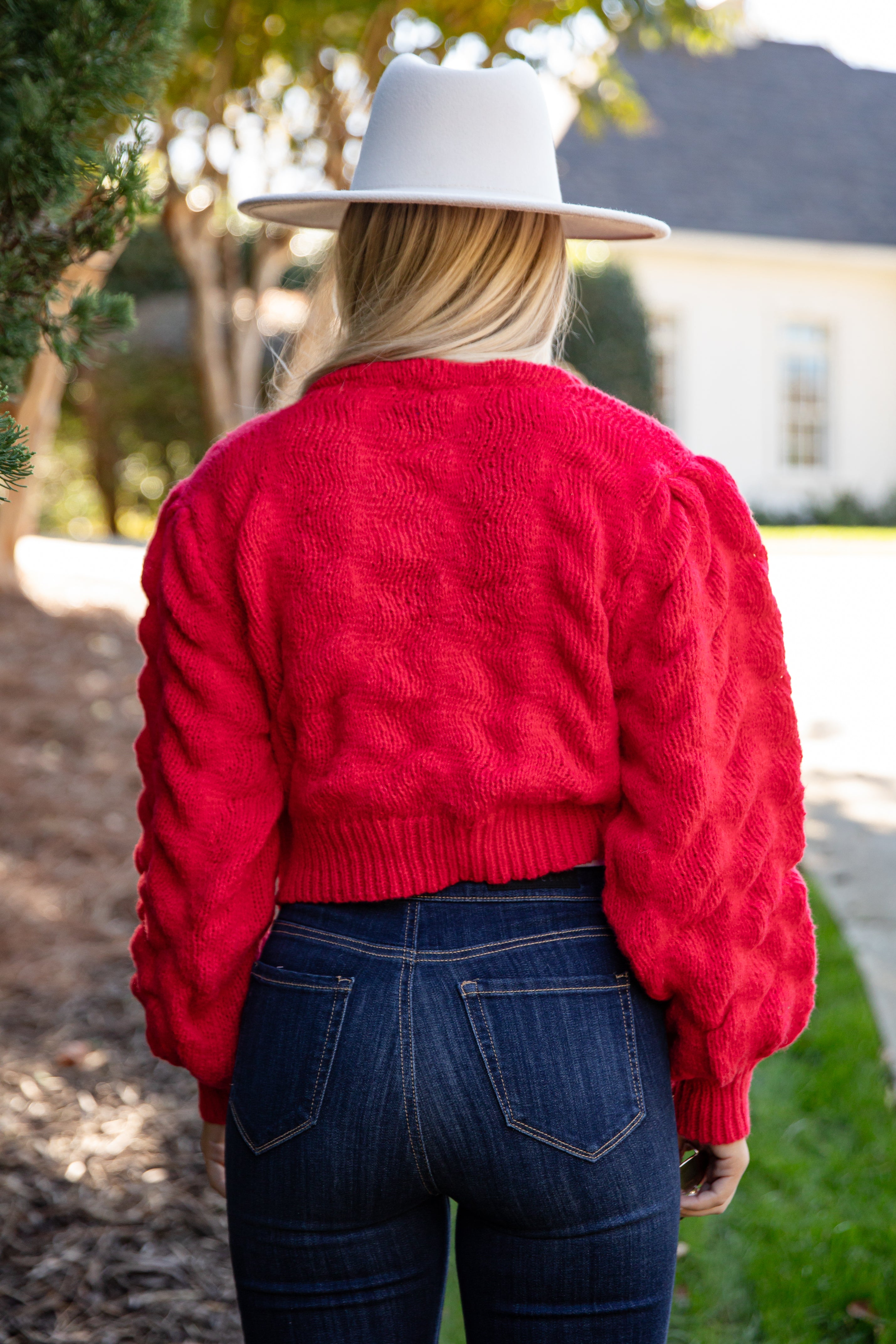 Person wearing a red sweater and white hat with a blurred outdoor background