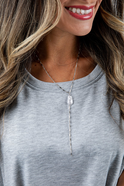 Woman wearing a gray top and a necklace with a clear pendant.