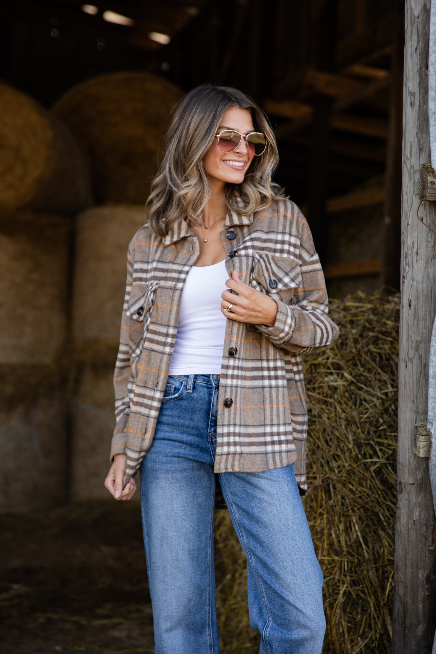 Woman wearing a plaid shirt and jeans standing in a barn with hay bales.