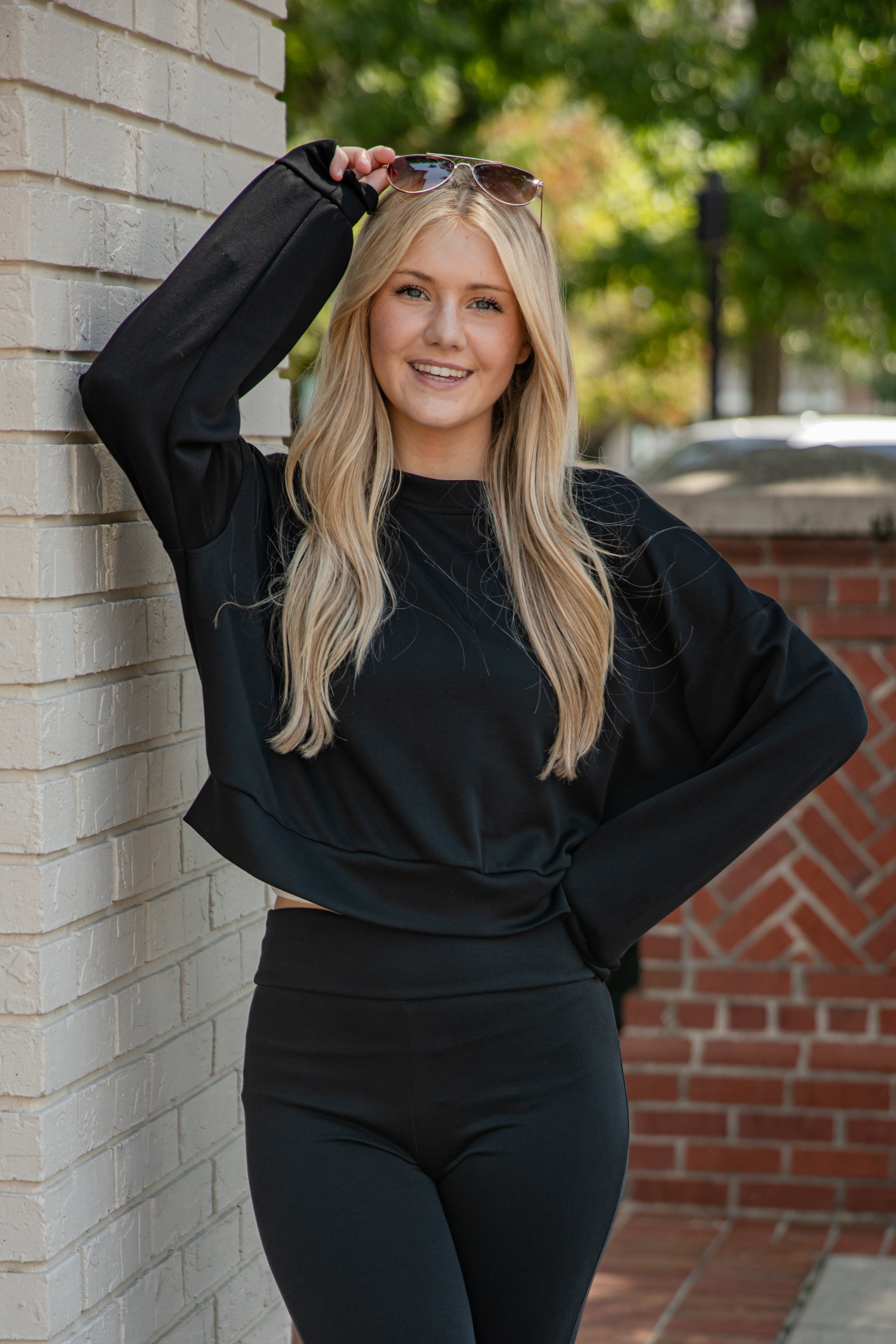 Woman in black outfit posing against a brick wall