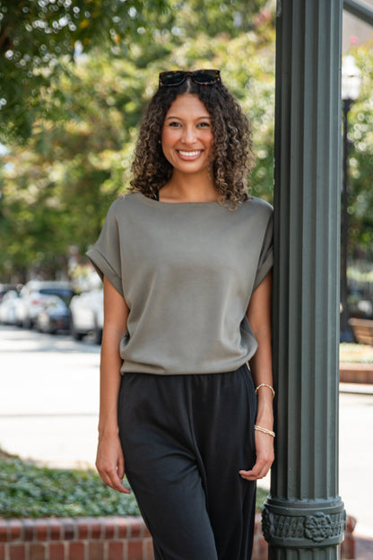 Woman in a gray top and black pants standing outdoors with trees and cars in the background