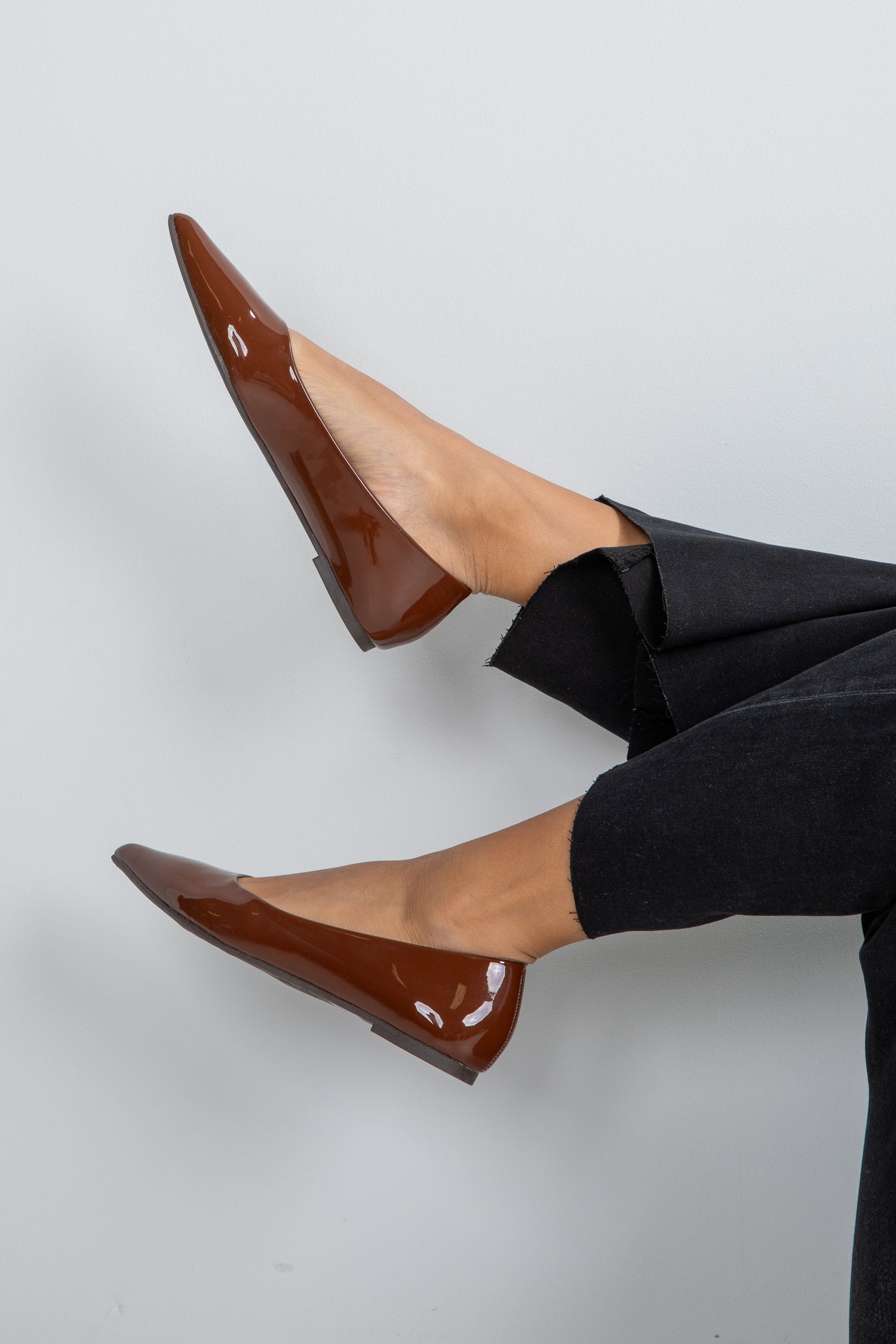 Brown patent leather shoes worn with black pants on a light gray background