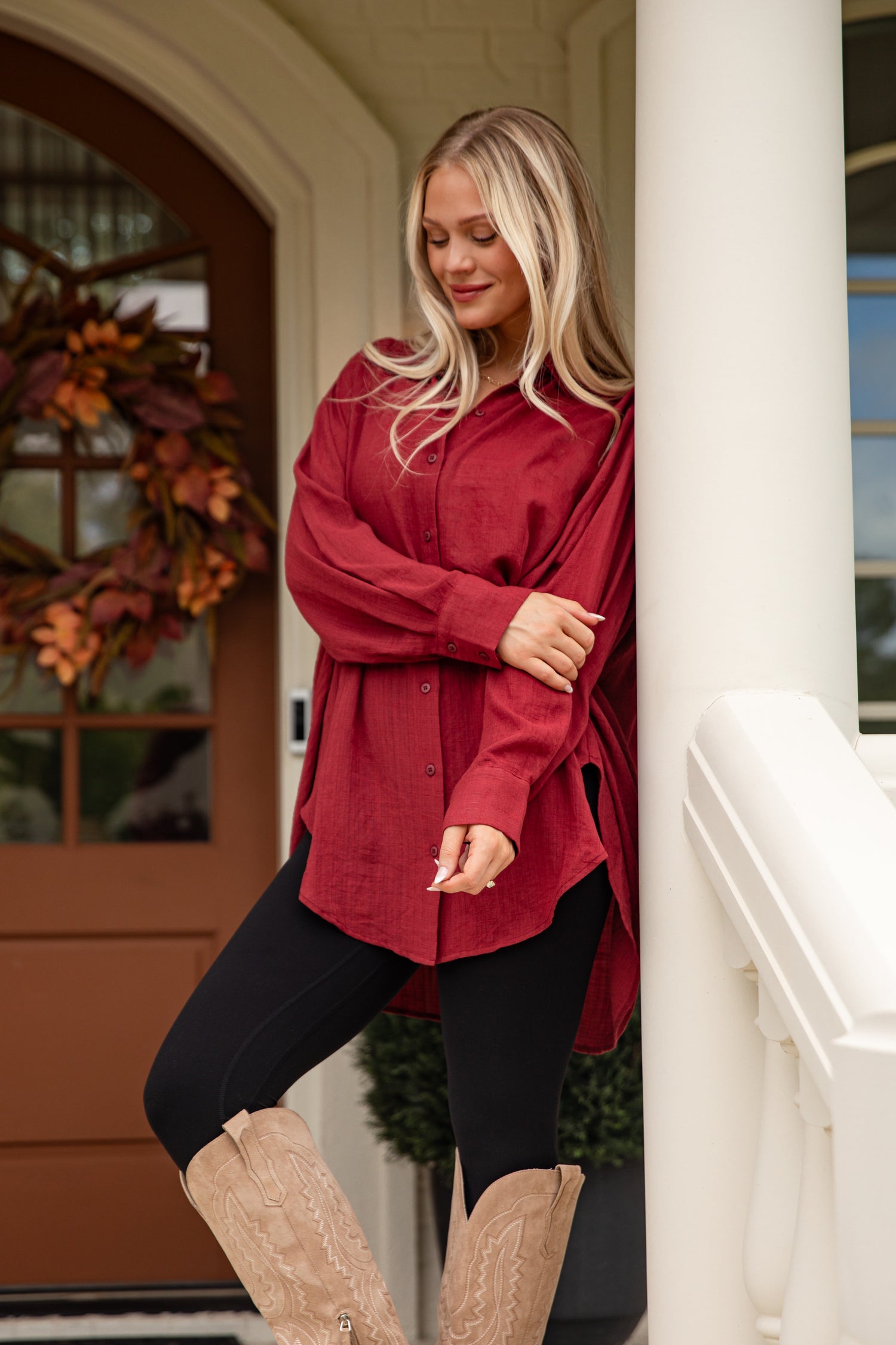 Woman in a red shirt and black pants standing in front of a house entrance.