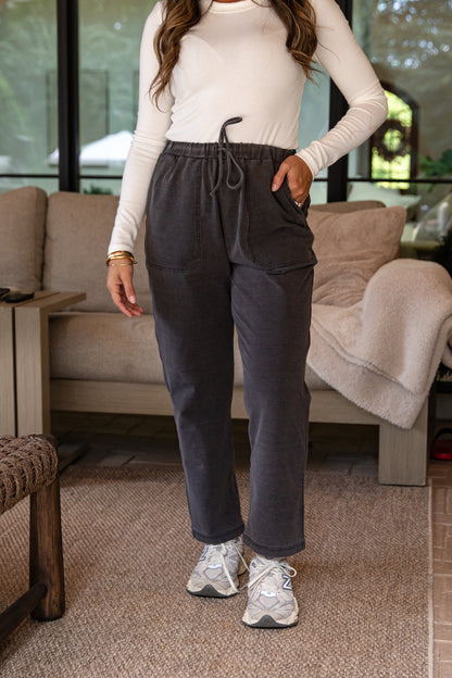 Person wearing a white long-sleeve top and dark gray sweatpants in a living room.