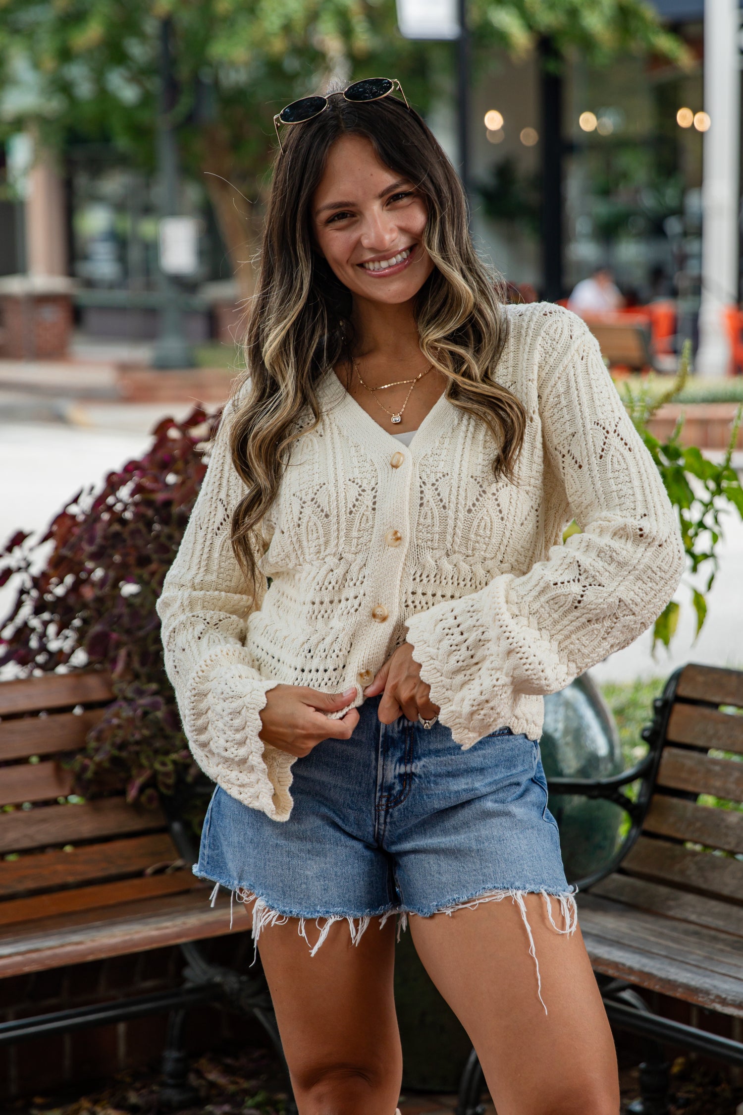 Woman wearing a cream cardigan and denim shorts standing outdoors.