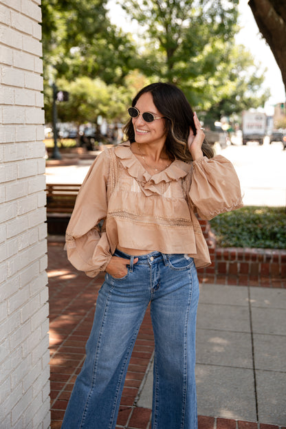Woman wearing a beige blouse with ruffles and blue jeans standing outdoors.