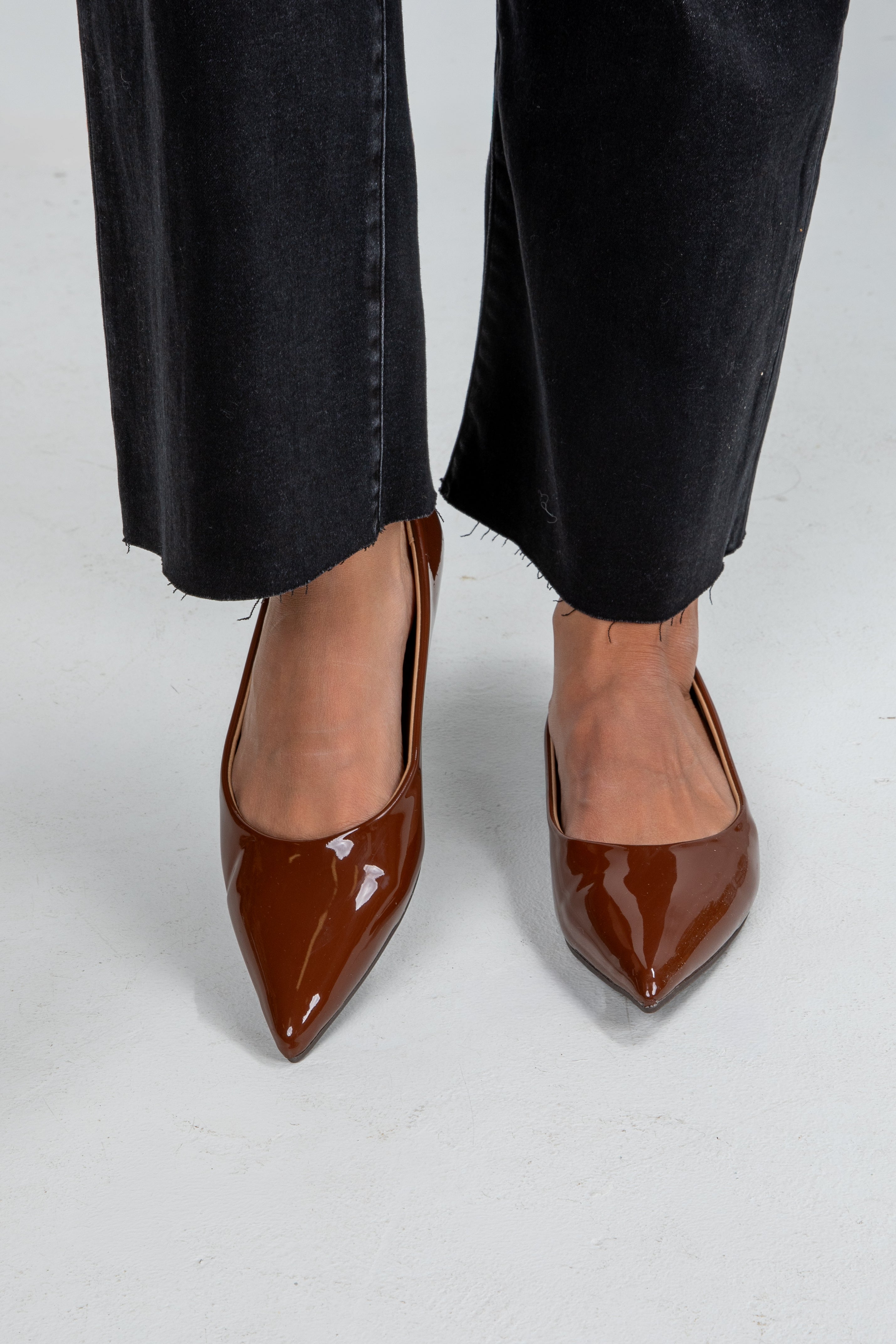 Brown patent leather shoes worn with black pants on a white background