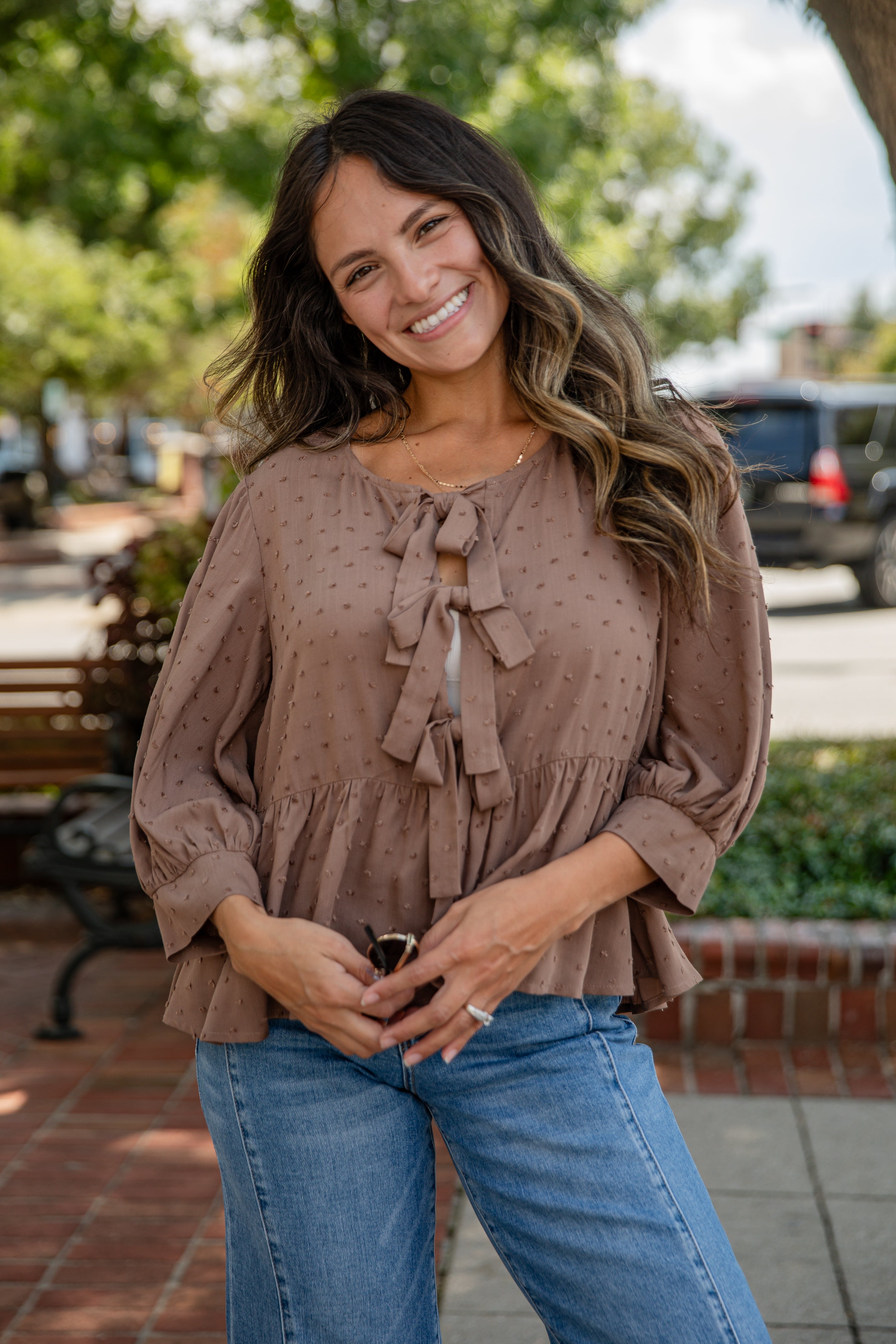 Woman wearing a brown blouse with ruffled sleeves and blue jeans standing outdoors.