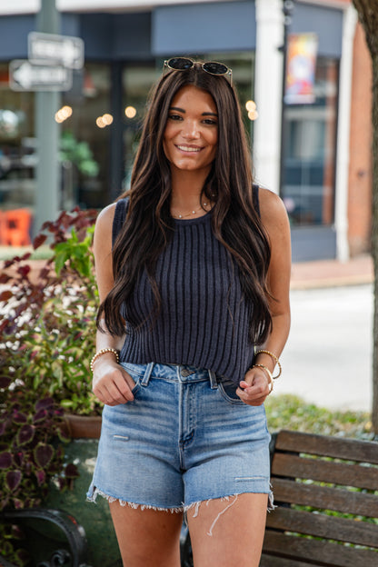 Woman wearing a dark ribbed top and denim shorts standing outdoors.