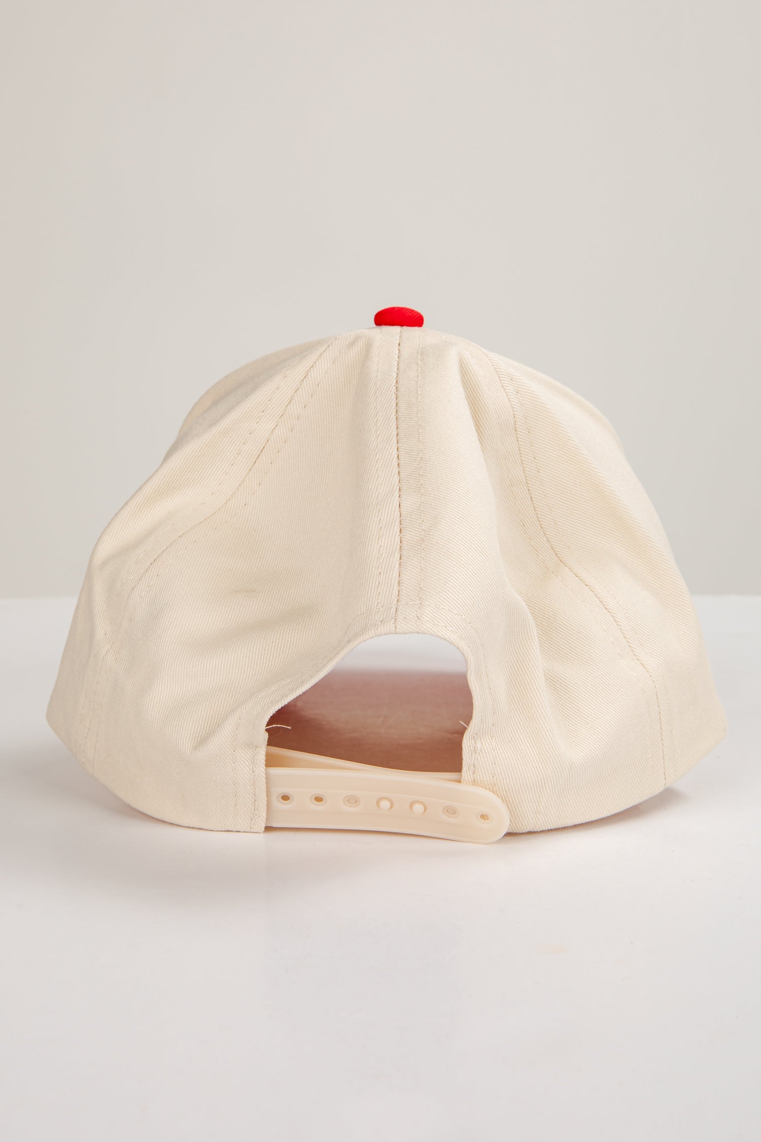 Beige baseball cap with a red button on a light gray background
