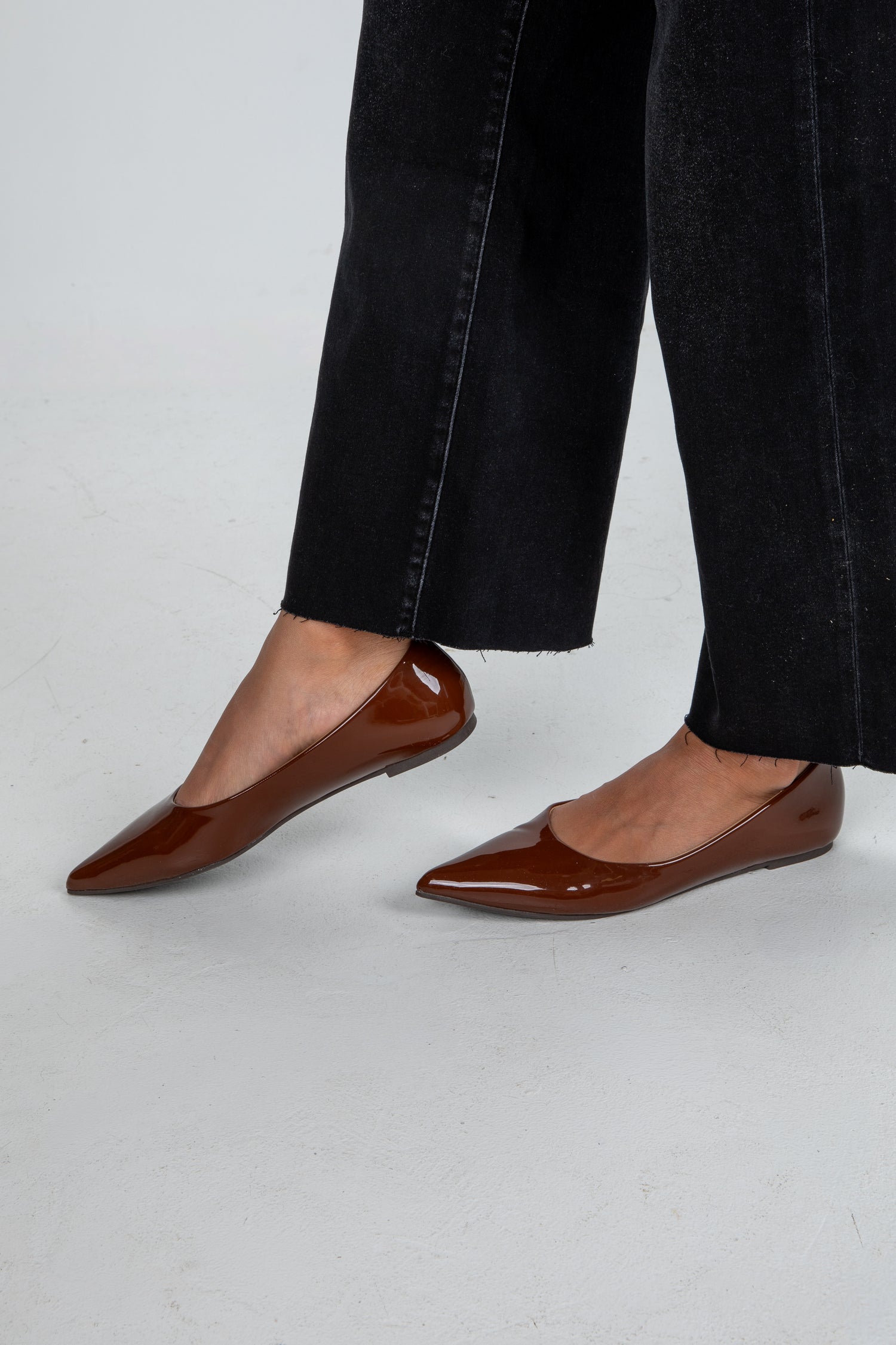 Brown pointed-toe flats worn with black jeans on a light gray background