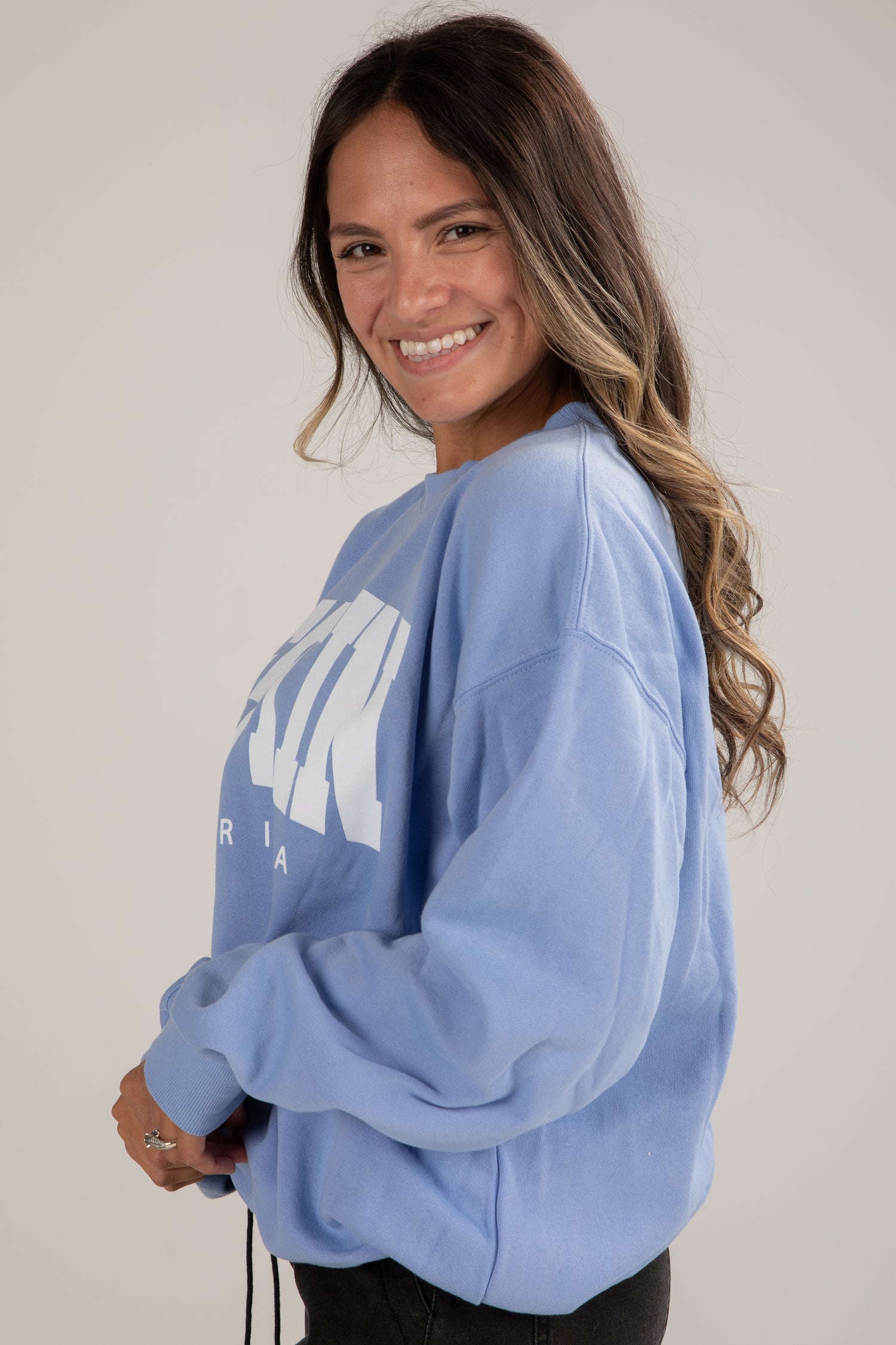 Woman wearing a light blue sweatshirt with a logo on a plain background