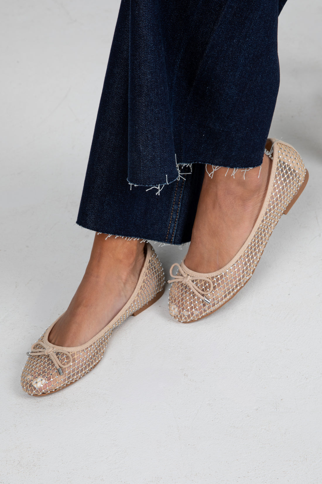 Beige mesh flats worn with dark jeans on a light gray background