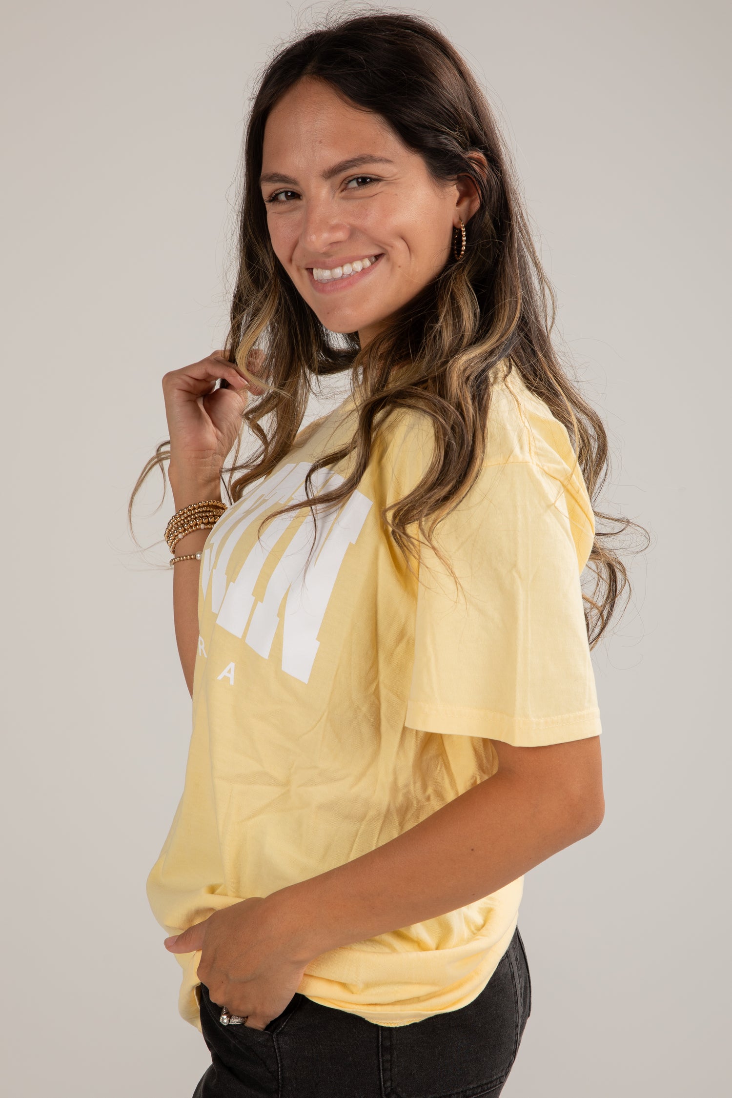 Woman wearing a yellow t-shirt with a white logo on a plain background