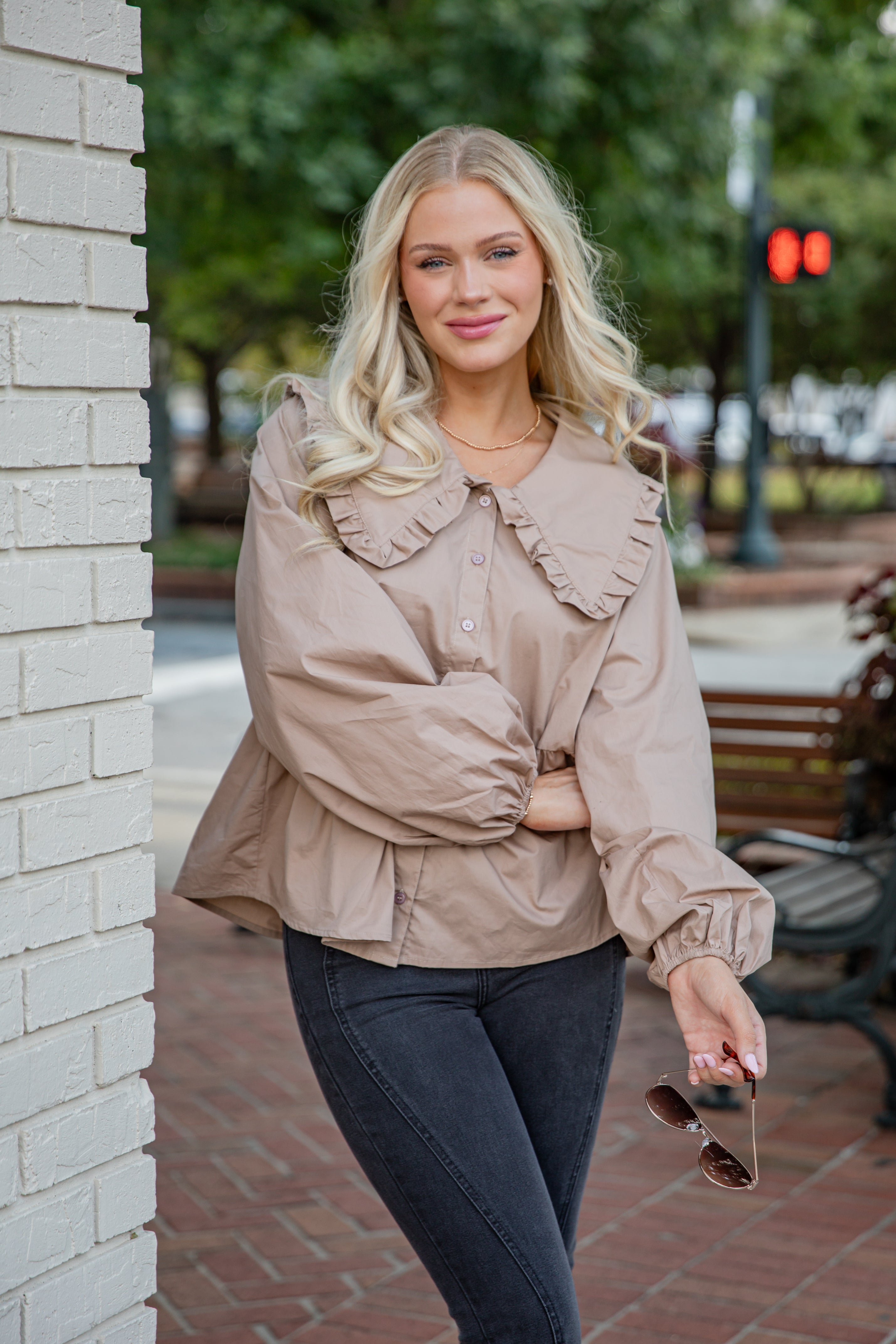 Woman wearing a beige jacket with ruffled details on a city street.