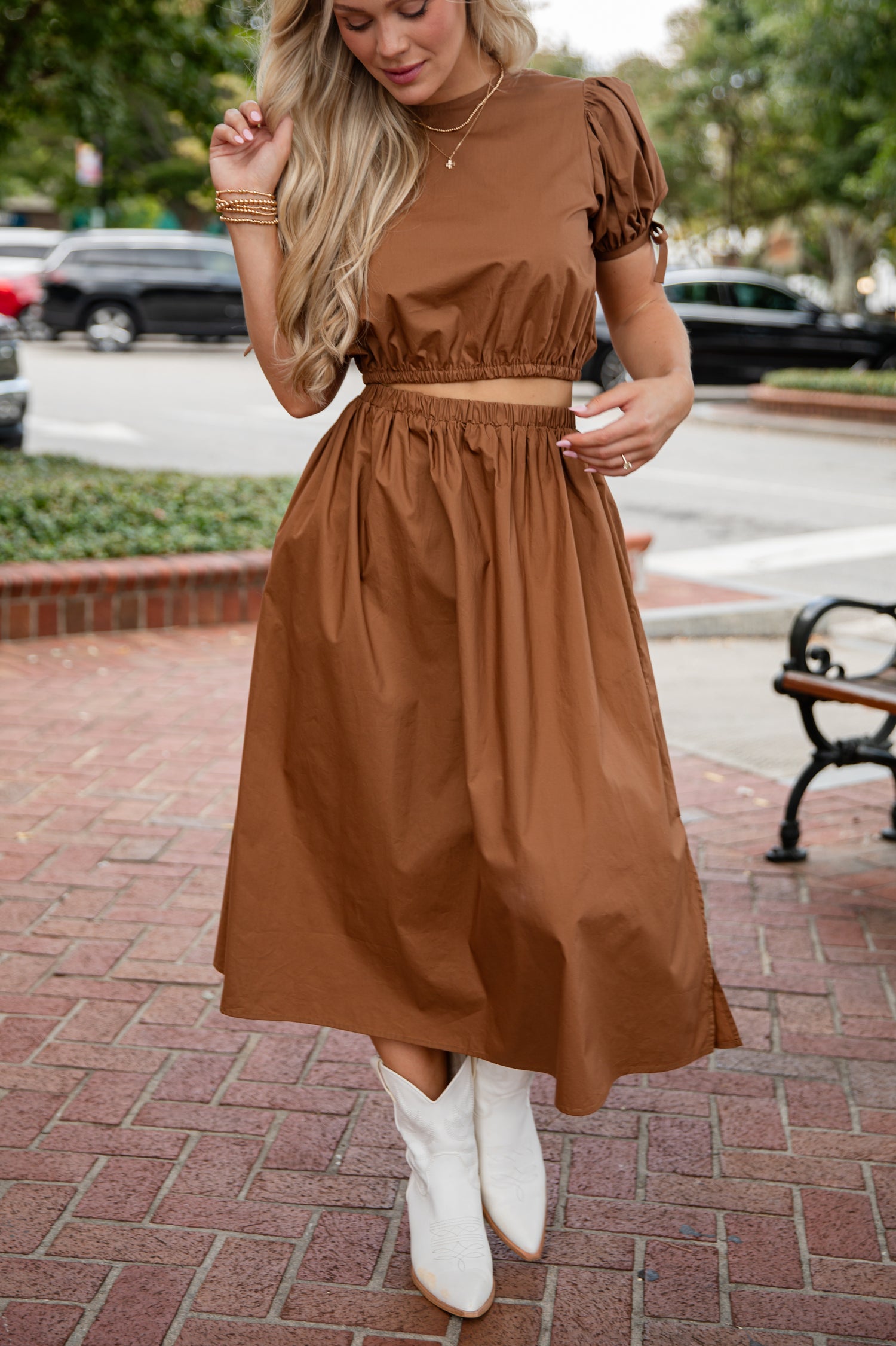 Woman wearing a brown dress with white boots on a city street.