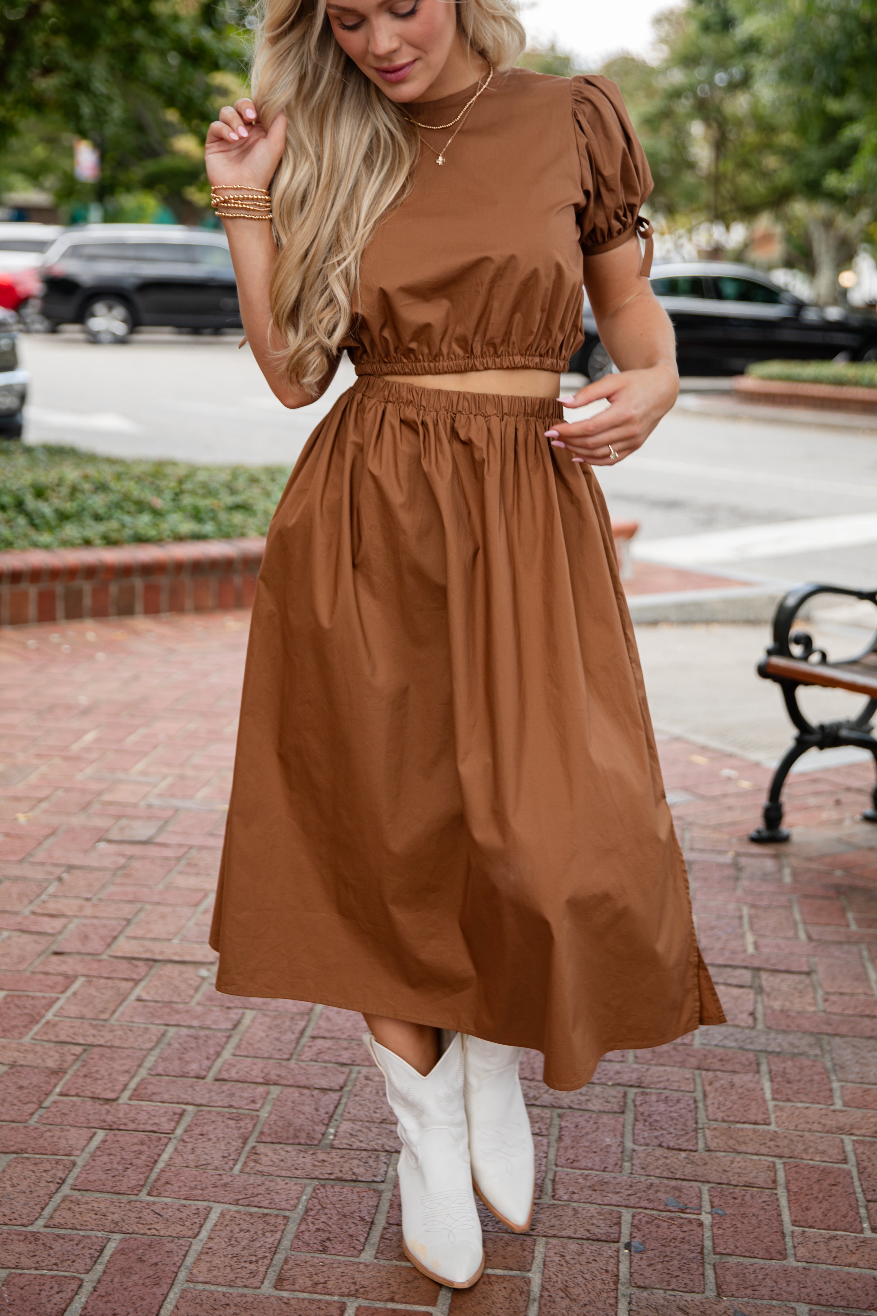 Woman wearing a brown dress with white boots on a city street.