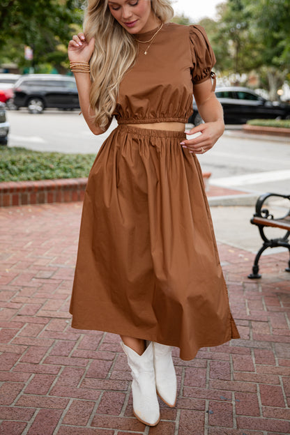 Woman wearing a brown dress with white boots on a city street.