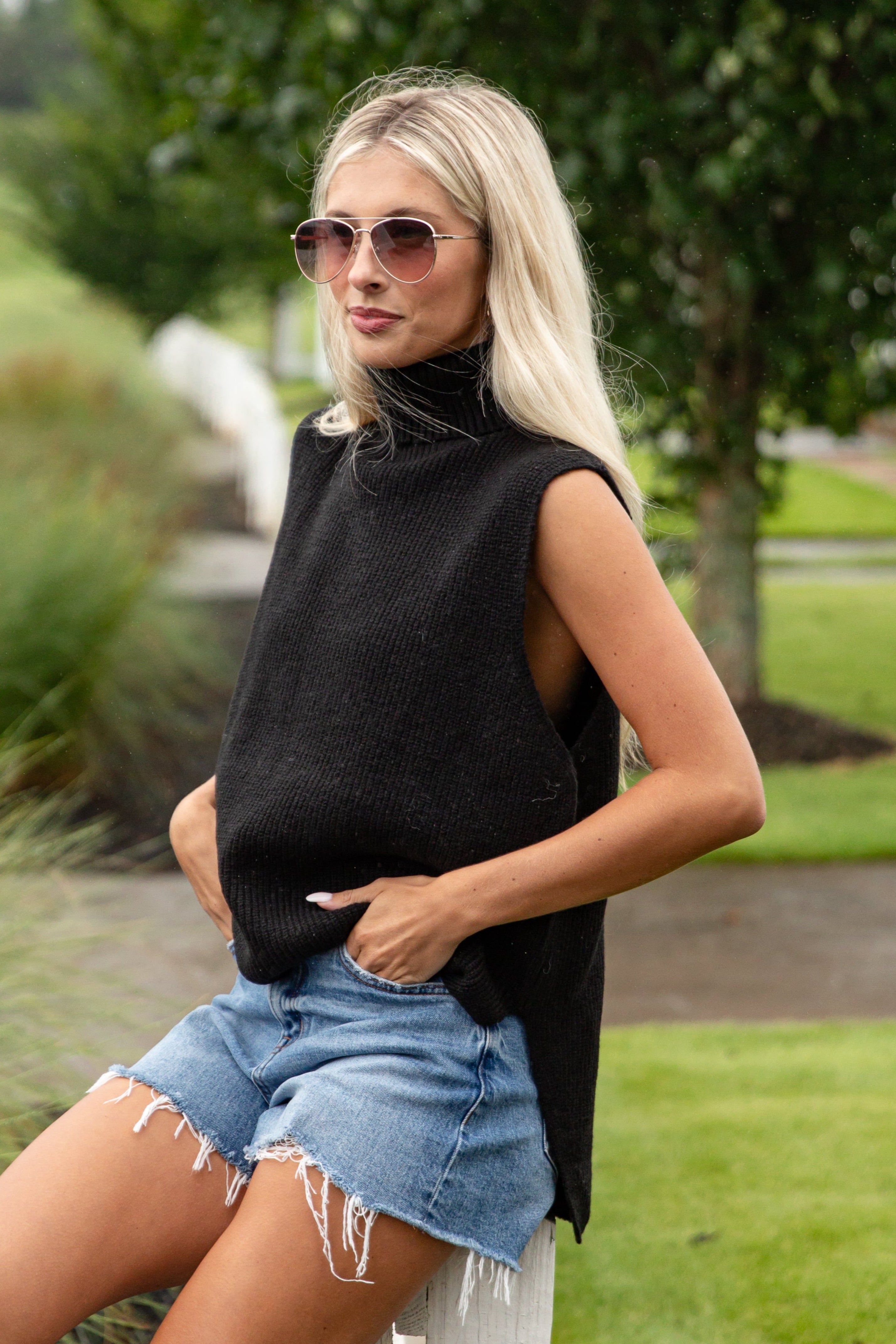 Woman wearing a black sleeveless top and denim shorts outdoors.