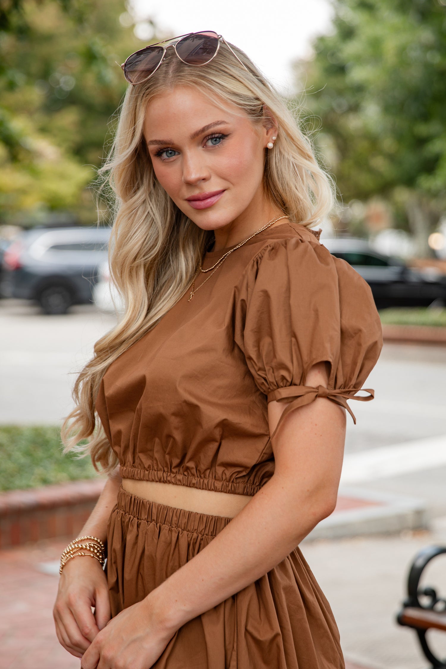 Woman in a brown outfit standing outdoors with trees in the background