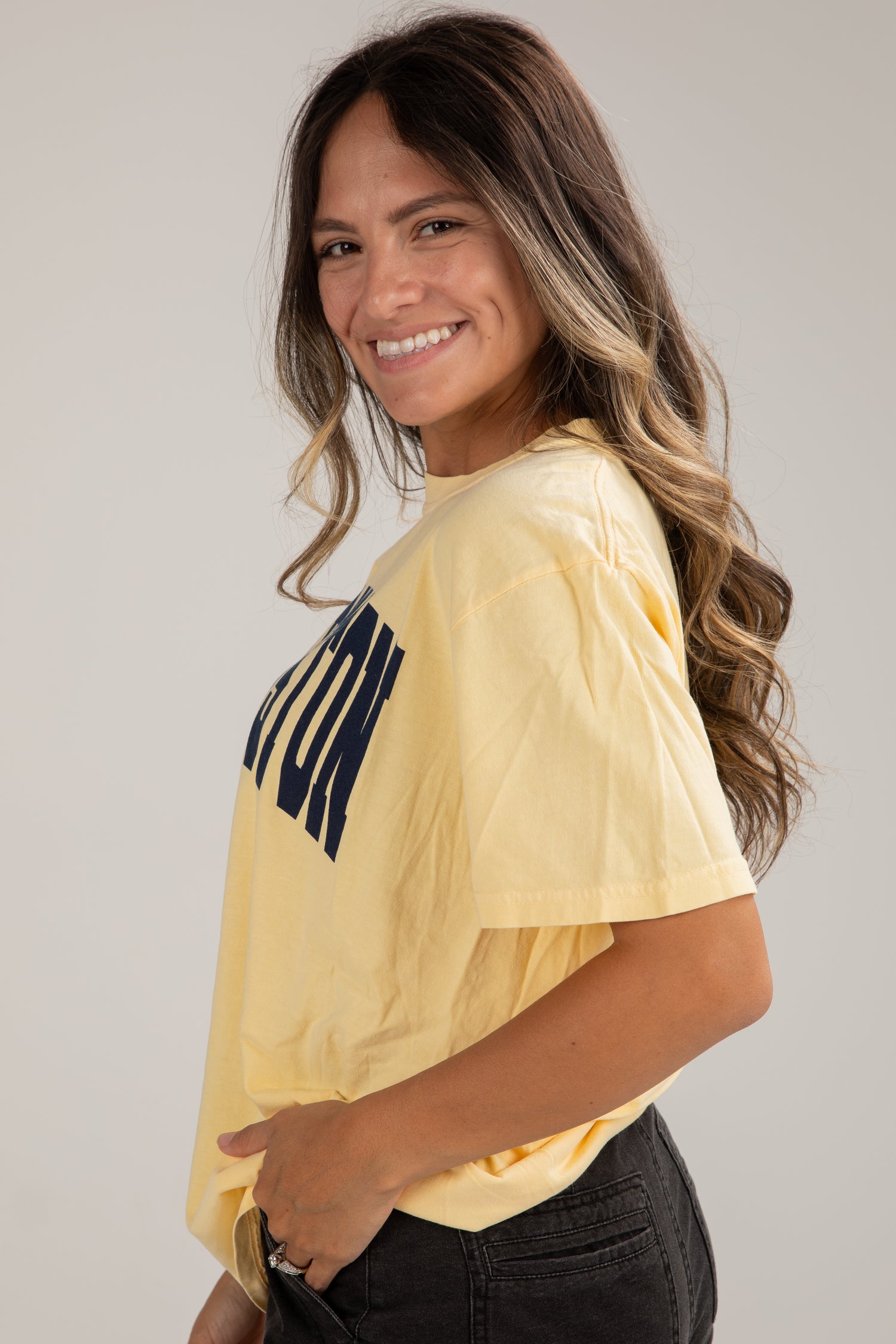 Woman wearing a yellow t-shirt with a logo on a plain background