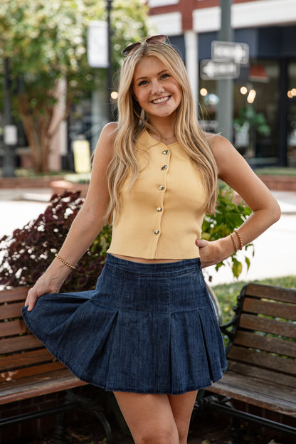 Woman in a yellow top and blue skirt sitting on a bench outdoors.