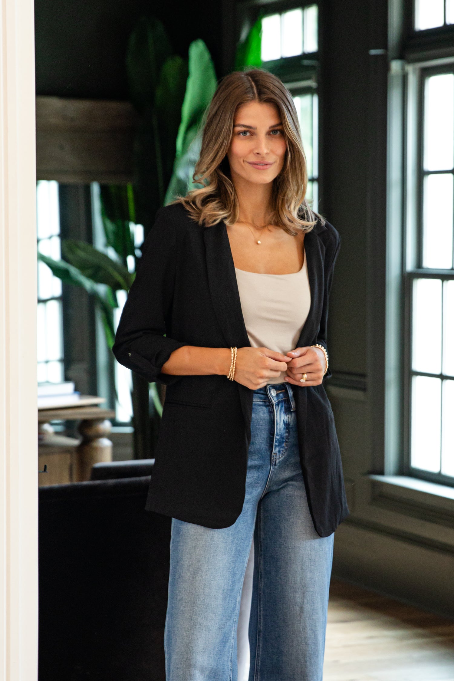 Woman wearing a black blazer, white top, and blue jeans indoors.