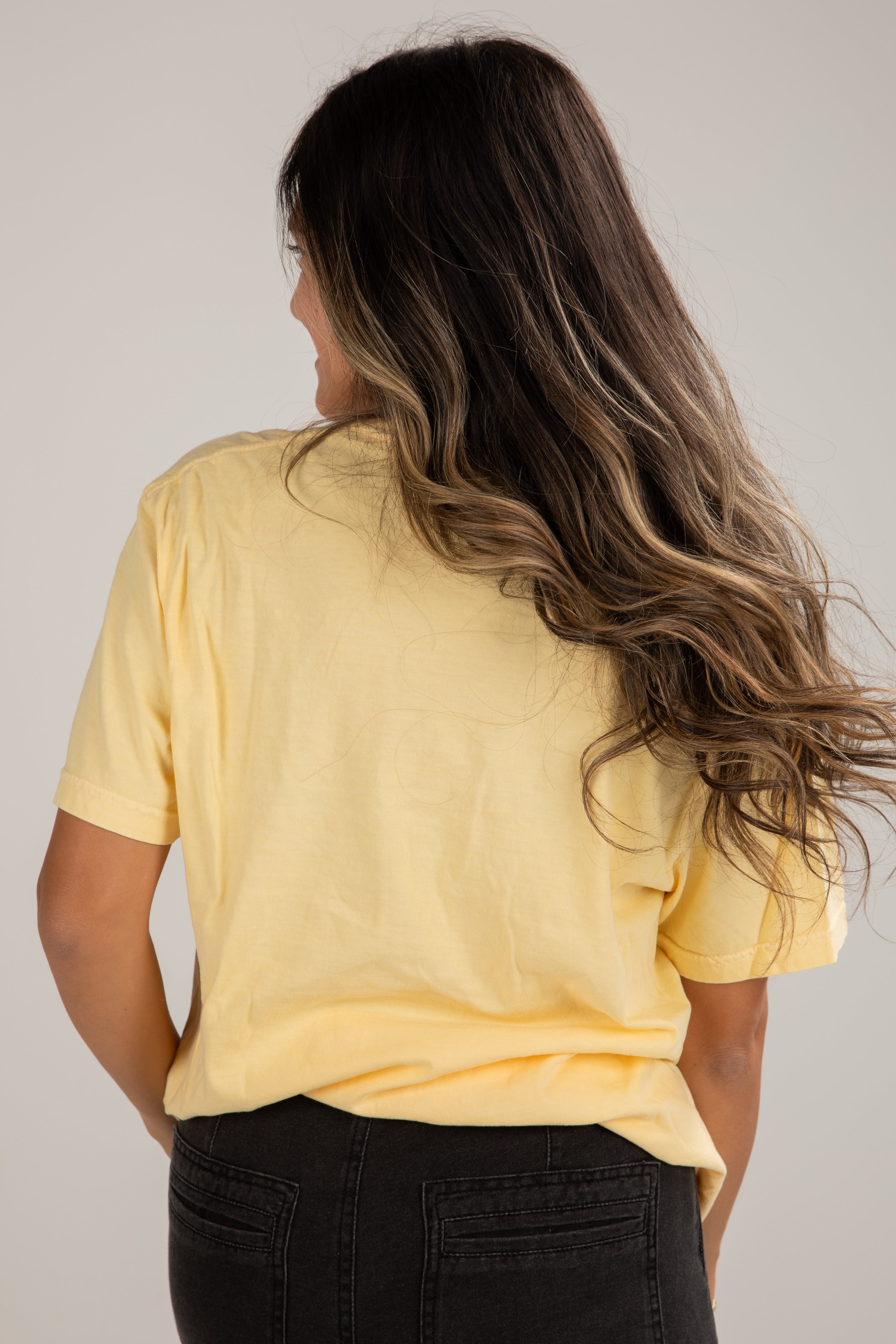 Person wearing a yellow t-shirt and black pants against a plain background